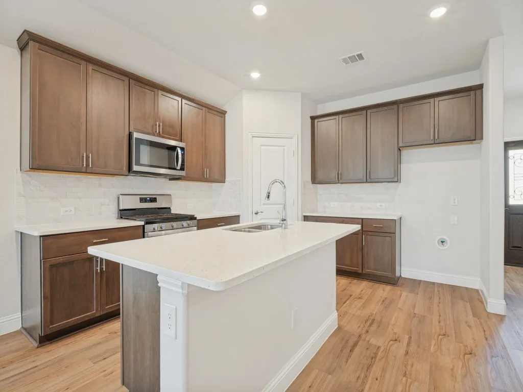Kitchen featuring an island with a light-toned countertop, stainless steel appliances, wood-finish flooring, recessed lighting, and dark wood cabinetry