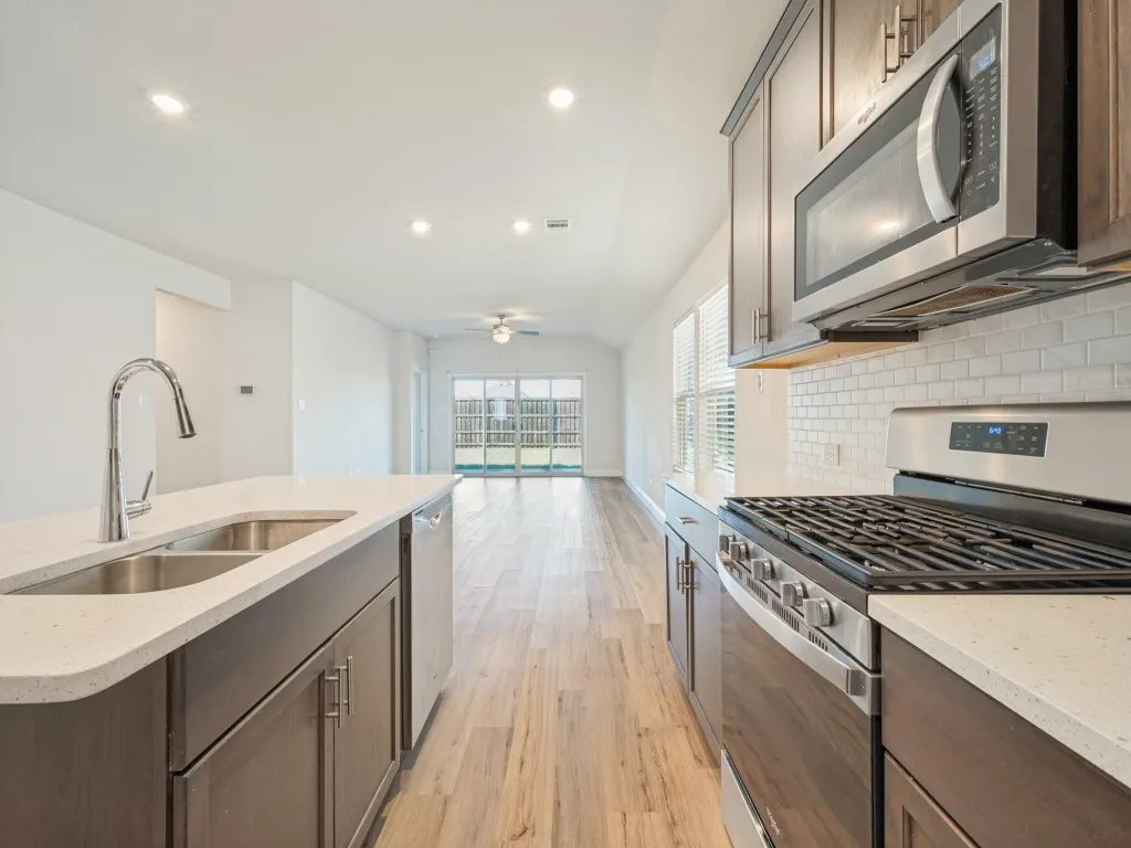 Kitchen featuring dark wood-finish cabinetry, light-colored countertops, stainless steel appliances, and a subway tile backsplash