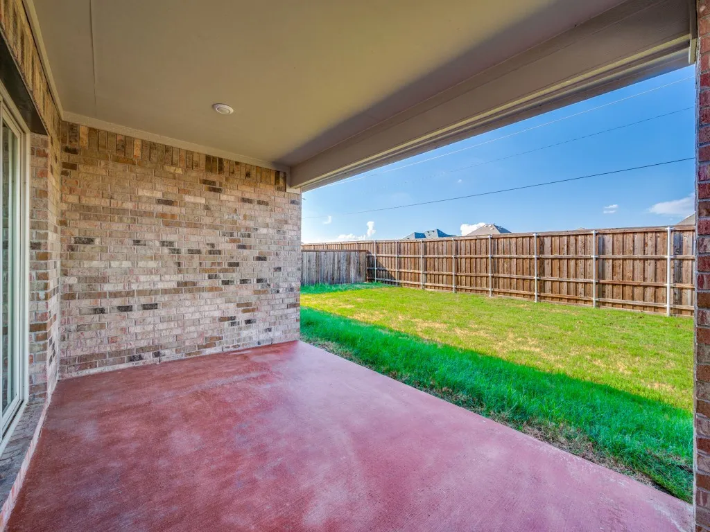 Covered patio with a stained concrete slab, brick exterior, and a fenced backyard with grass