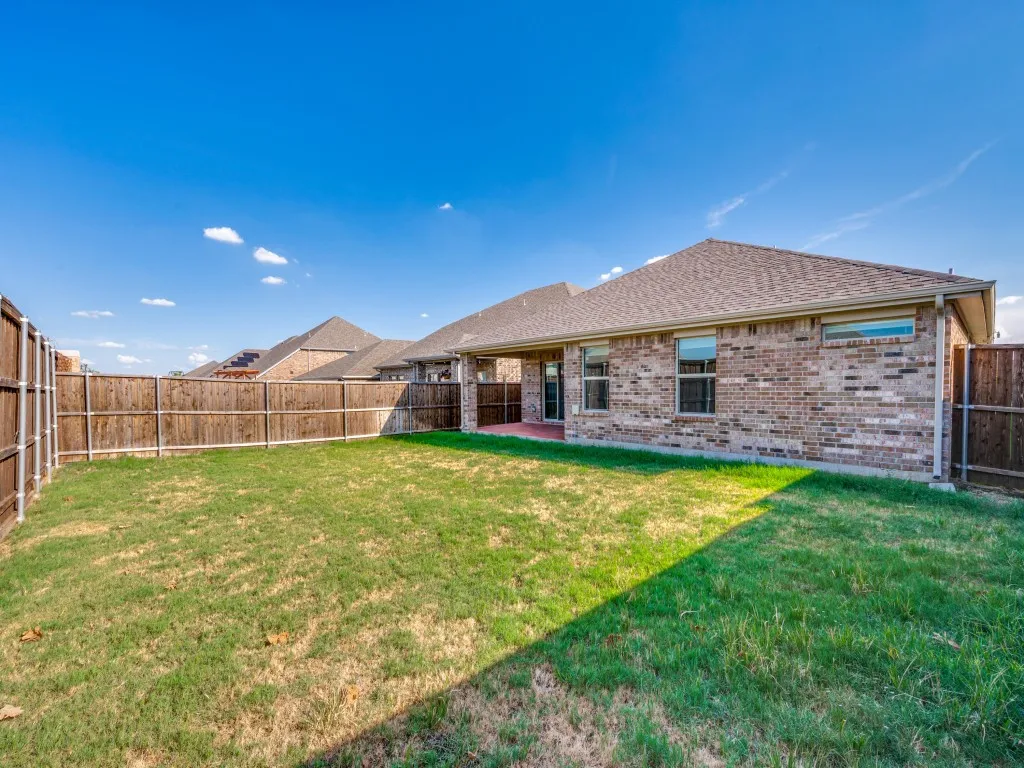Expansive backyard featuring a natural wood privacy fence, a brick exterior, and a covered patio
