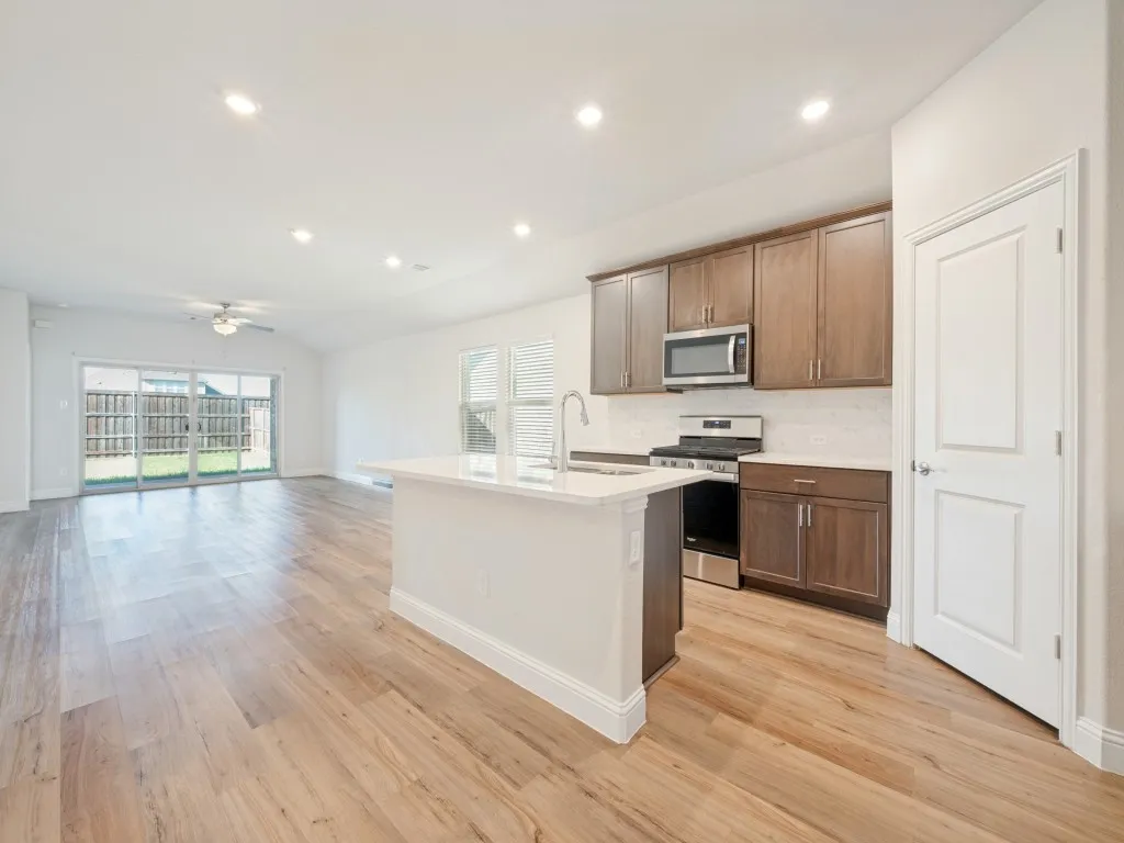 Open-concept kitchen with a central island, wood-finish flooring, stainless steel appliances, and sliding glass doors to the backyard