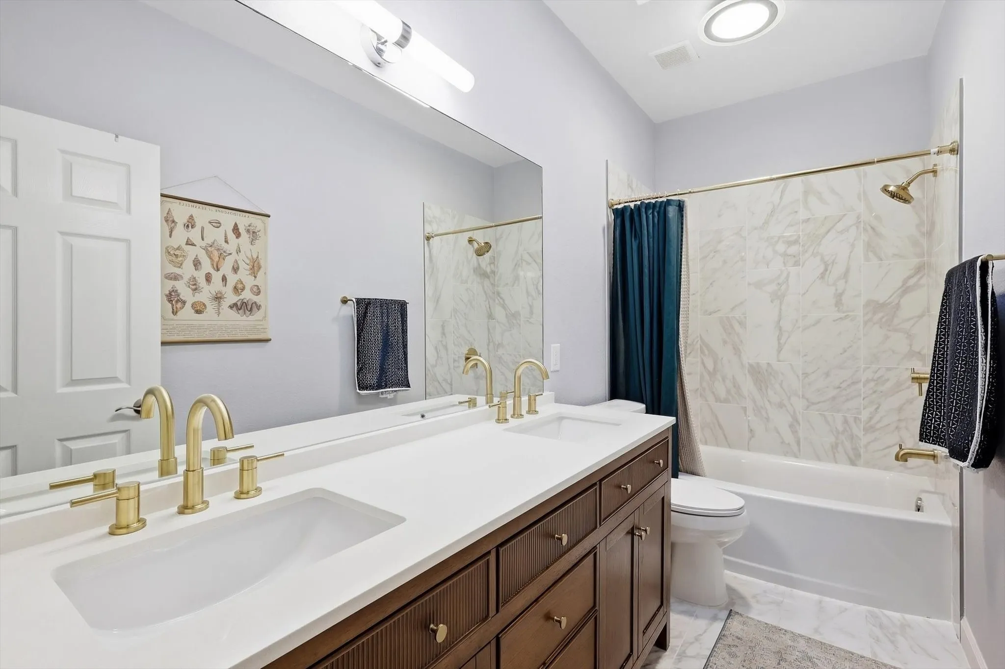 BEAUTIFUL UPDATED secondary full bathroom with lovely tiled shower-tub, quartz counters, double vanity, gold accents, wooden fluted cabinets providing LOADS of storage space, plus decorative and overhead lighting