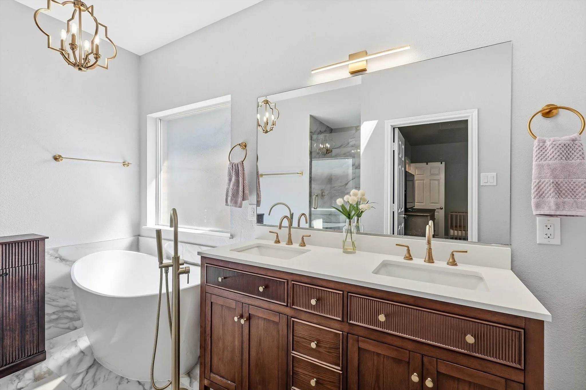 UPDATED primary ensuite bath with beautiful and functional fluted wooden cabinets, double vanity, quartz countertops, gold hardware accents, towel holders, and decorative lighting