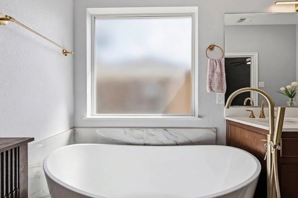 UPDATED primary ensuite bathroom features a gorgeous free standing tub, gold accents and a frosted window, allowing natural light in while maintaining privacy