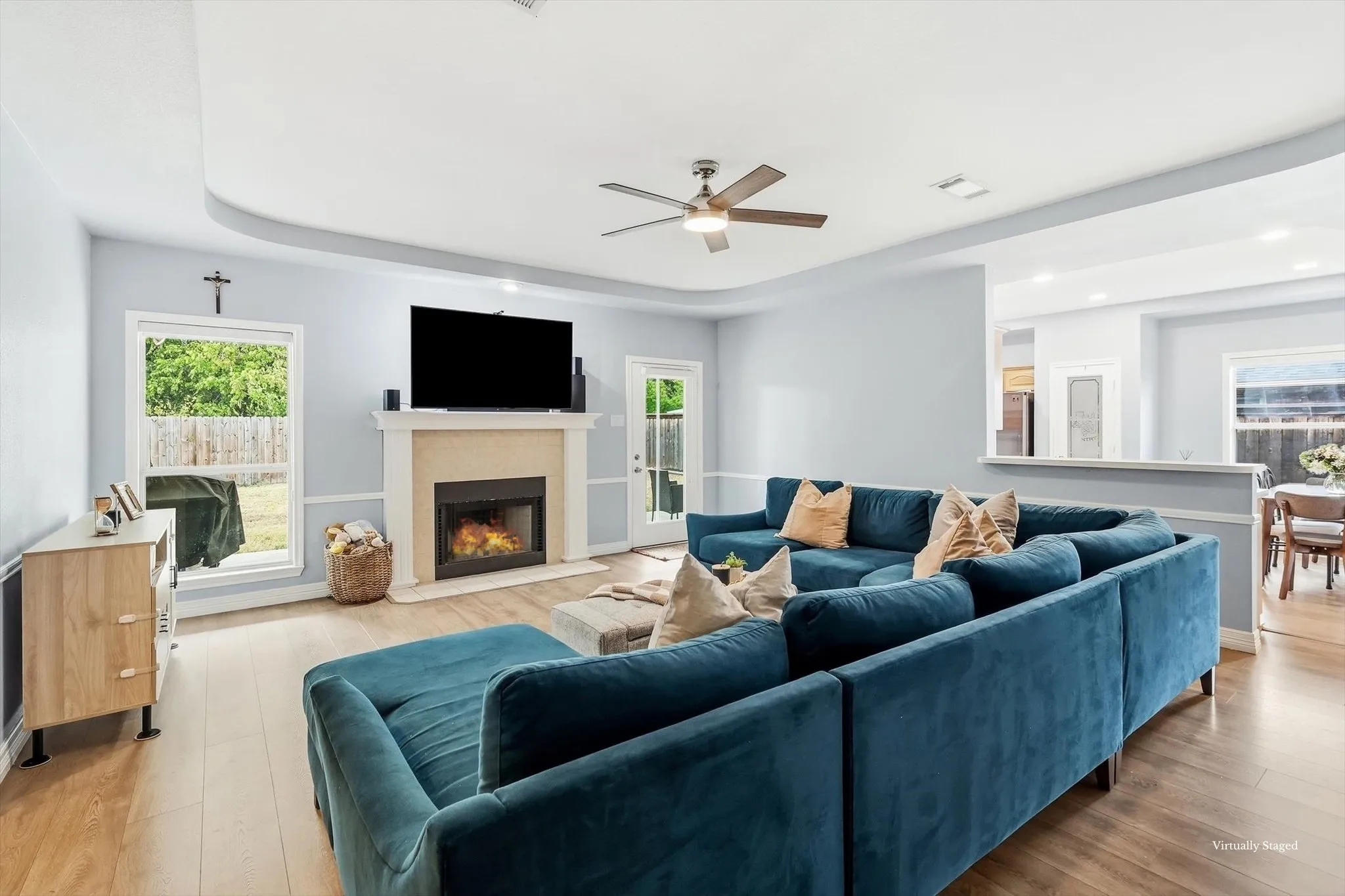Light and bright living room with ceiling fan, wood burning fireplace, and tray ceilings