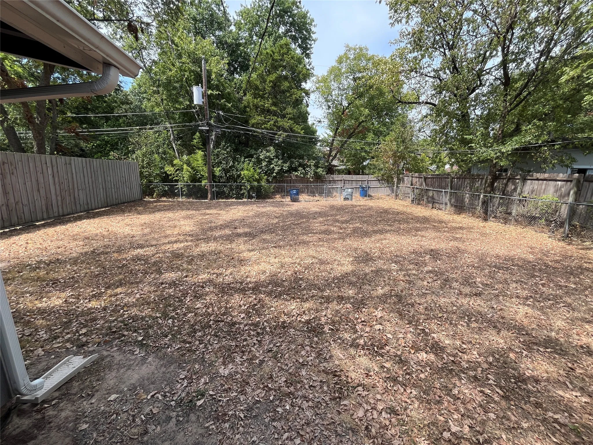 Expansive backyard featuring a combination of wood and chain-link fencing, mature trees, and a gutter system