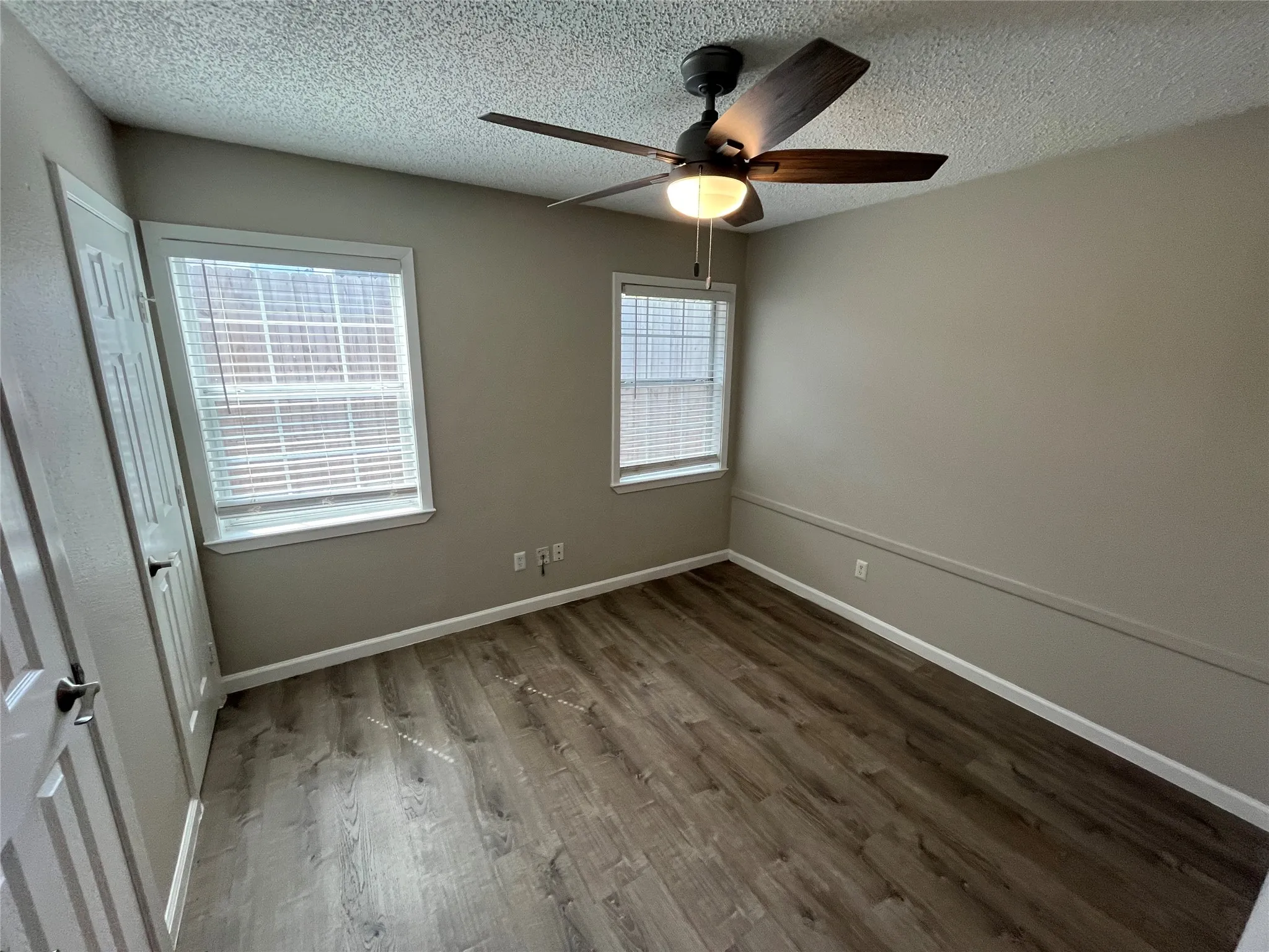 Wood-finish flooring, two windows with blinds, and a ceiling fan with light fixture