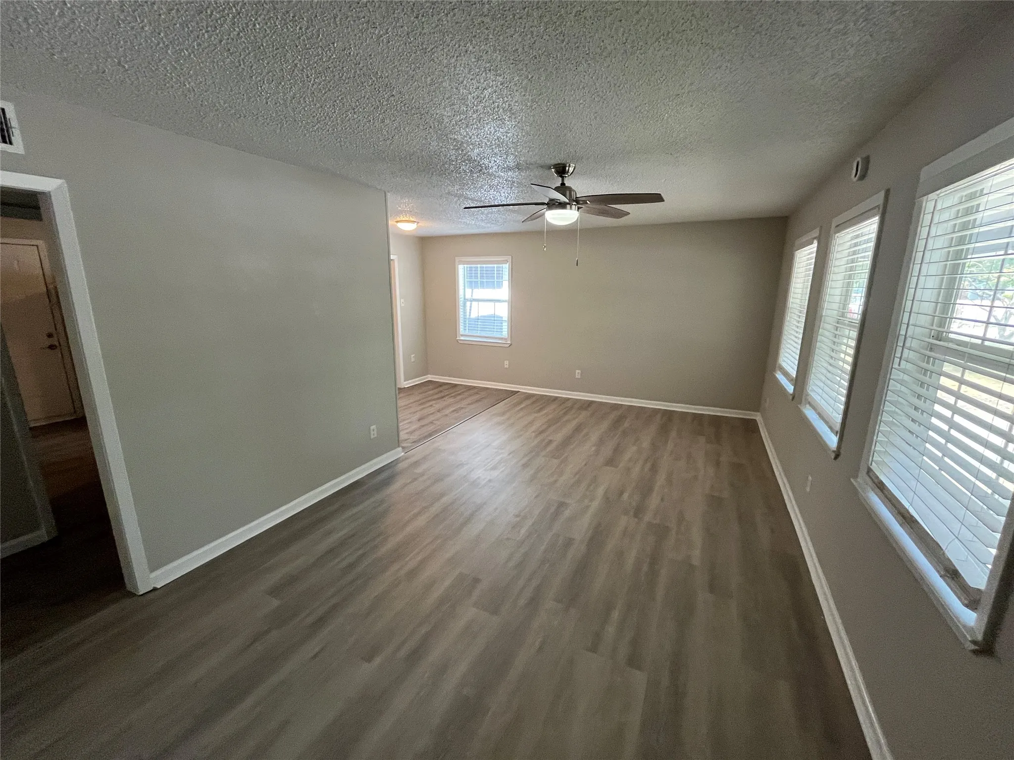 Wood-finish flooring, multiple windows with blinds, neutral wall tones, and a ceiling fan with integrated lighting