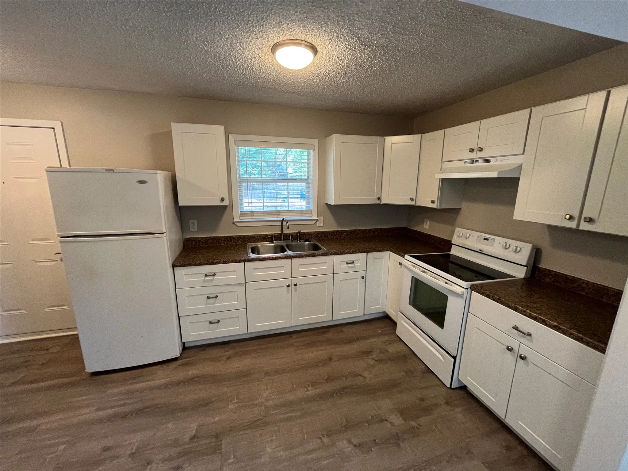 Wood-finish flooring, white cabinetry with silver hardware, dual-basin stainless steel sink, white electric range, and dark-toned countertops