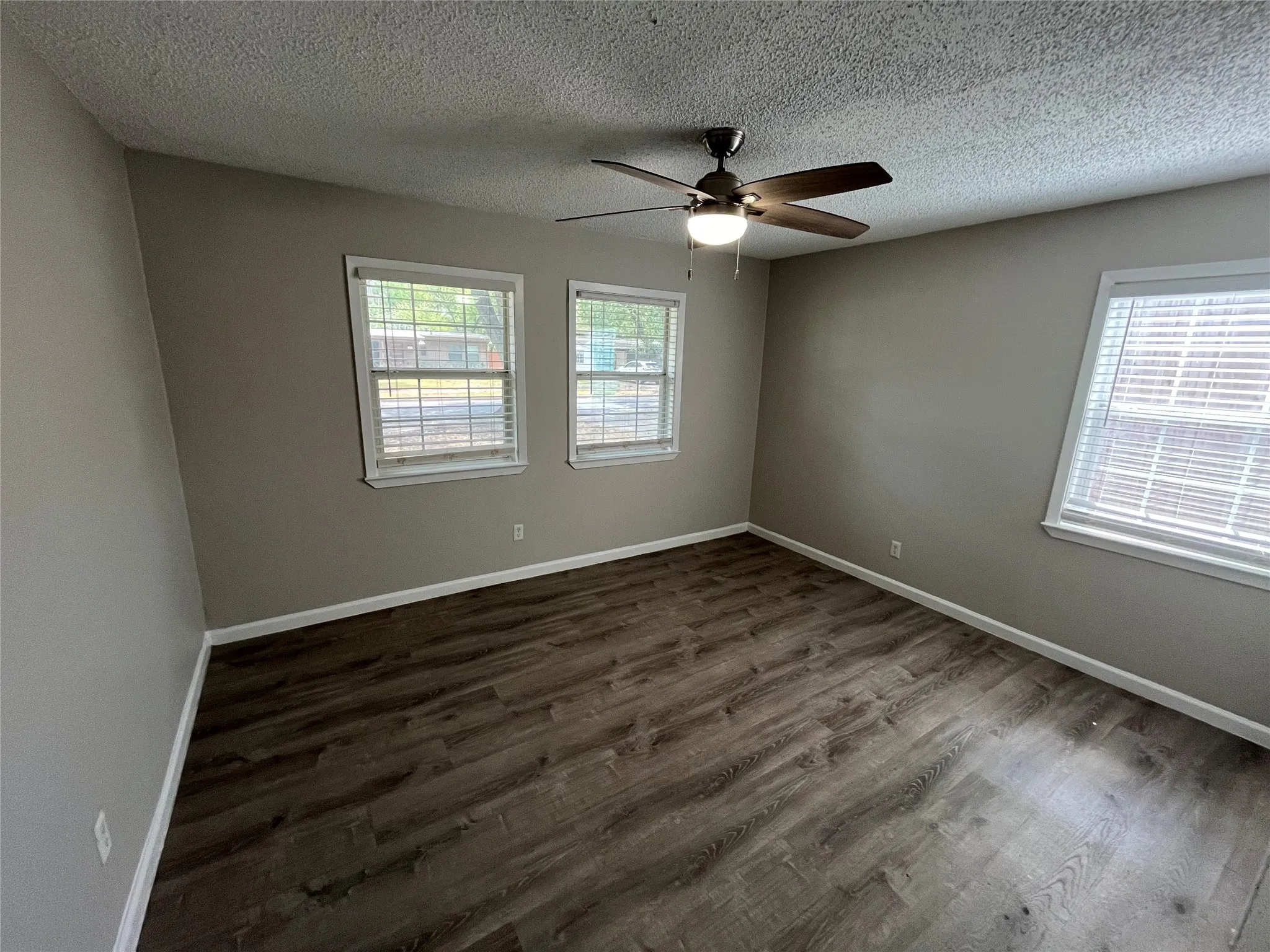 Room featuring wood-finish flooring, two windows with blinds, a ceiling fan with integrated lighting, and neutral-toned painted walls