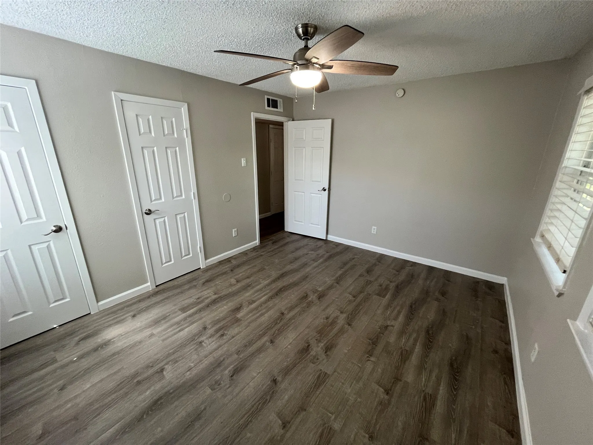 Wood-finish flooring with a neutral paint scheme, ceiling fan with integrated lighting, and white paneled doors