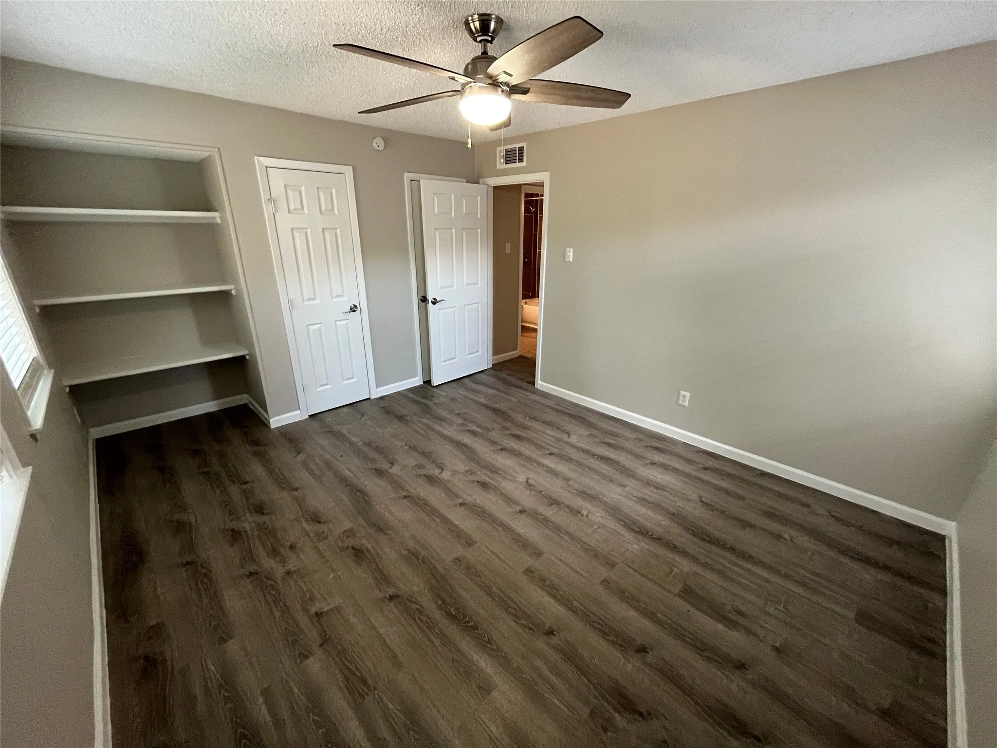 Wood-finish flooring, built-in shelving, ceiling fan with integrated lighting, and multiple panel doors