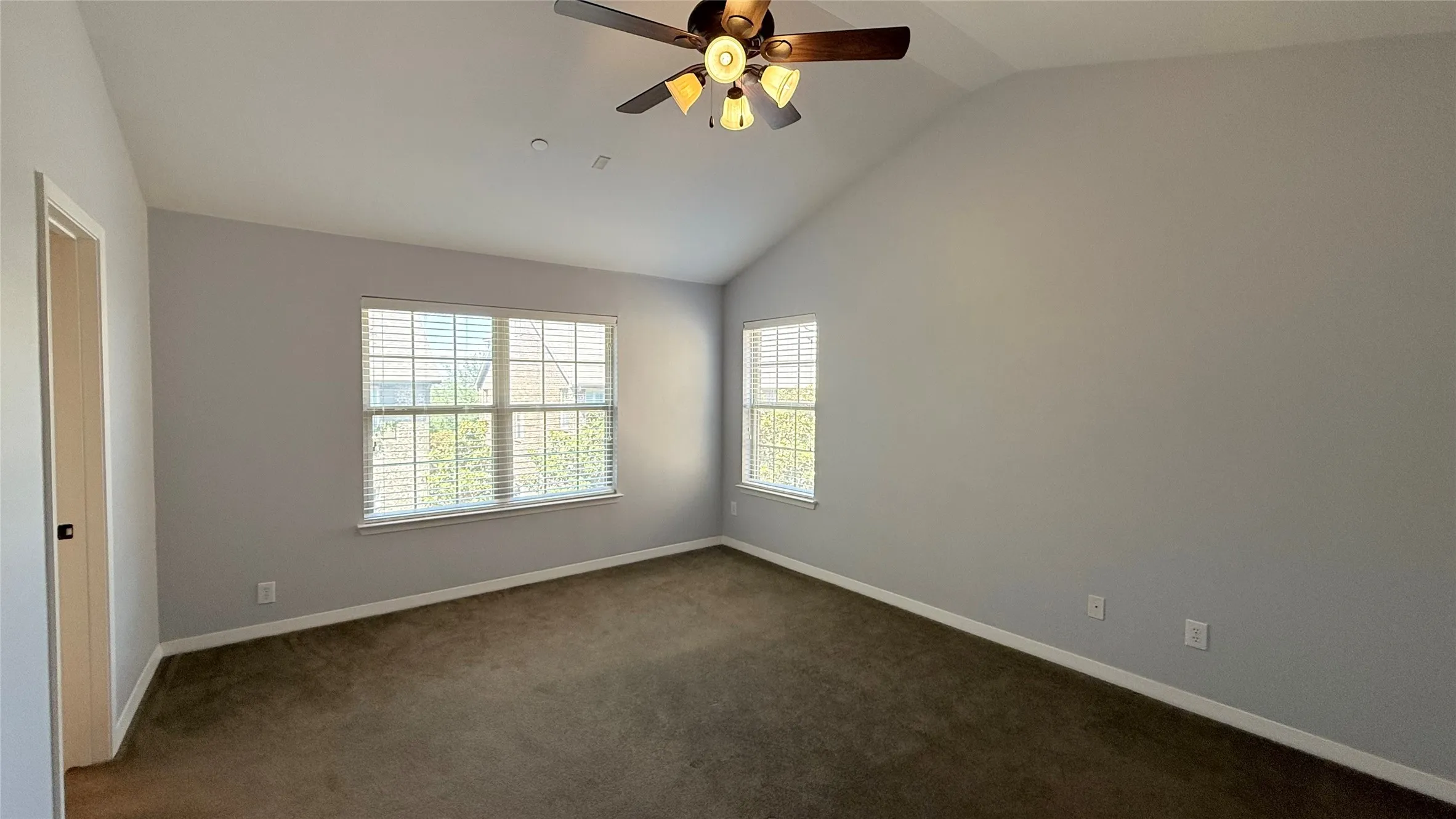 Vaulted ceiling, ceiling fan with light fixture, carpet flooring, two windows with blinds