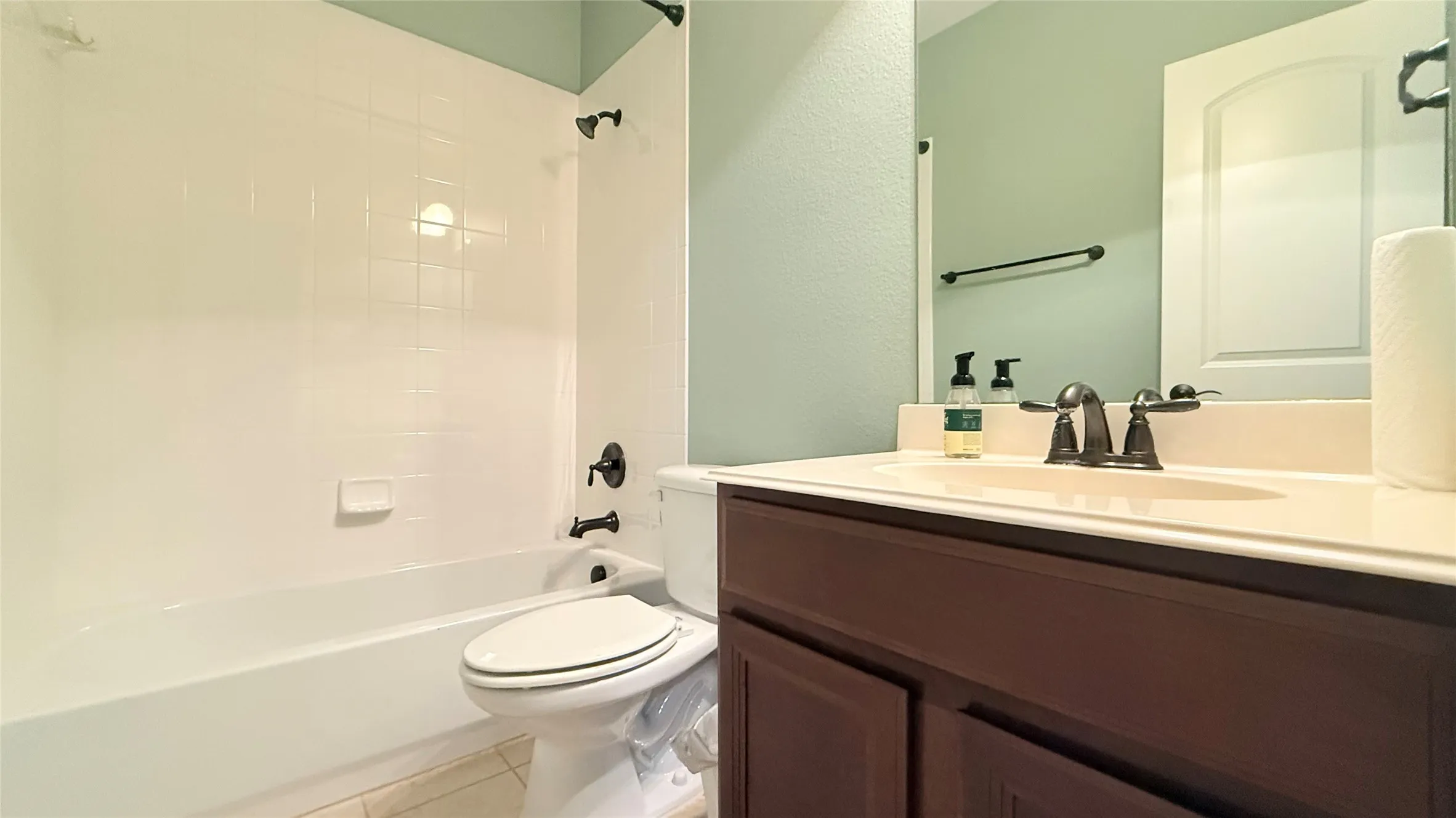 Bathroom with a white bathtub and shower surround, dark bronze fixtures, a vanity with a white countertop, and integrated sink