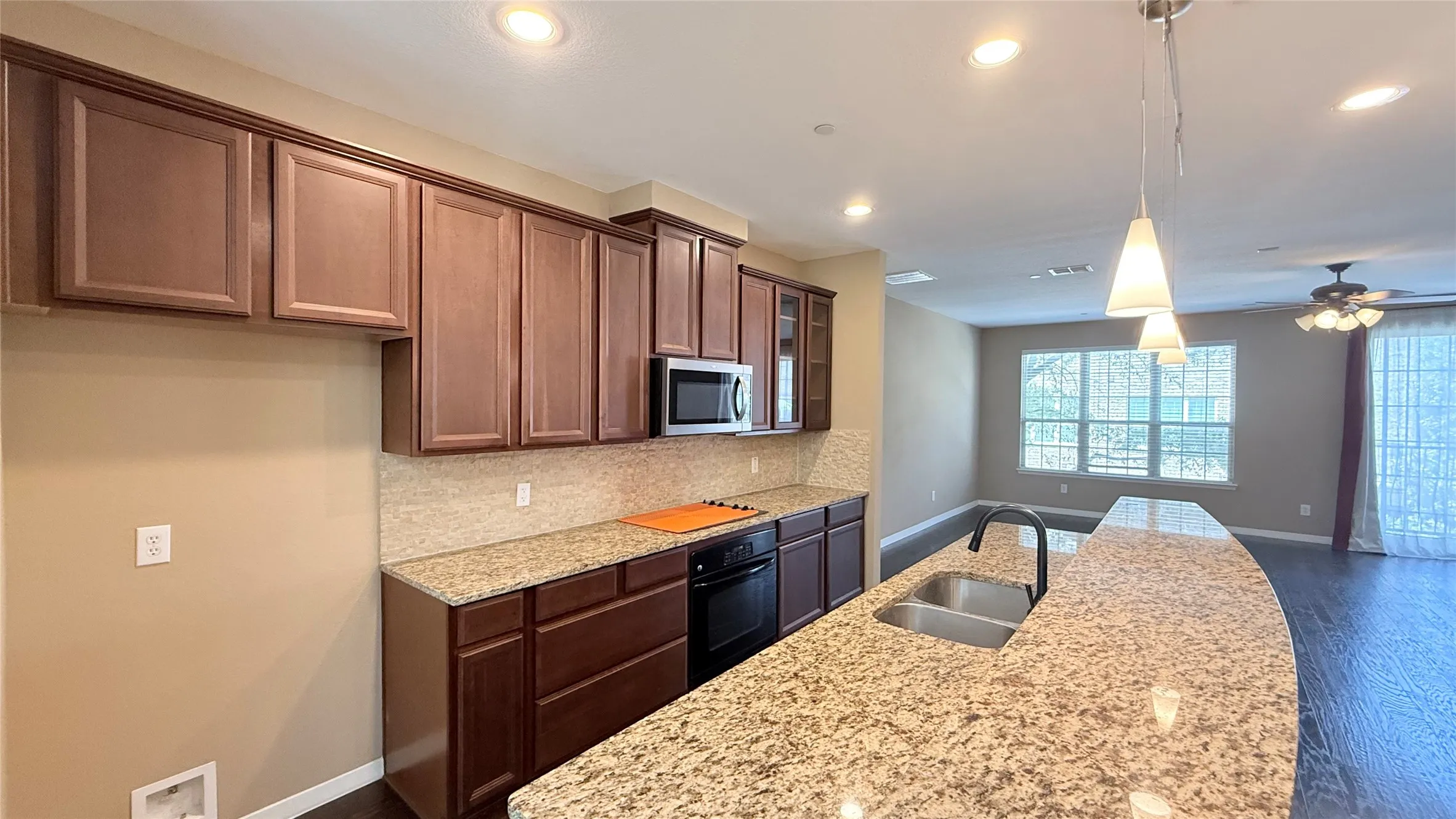 Kitchen featuring a curved granite-finish island with an undermount double-basin sink, pendant lighting, and recessed ceiling lights