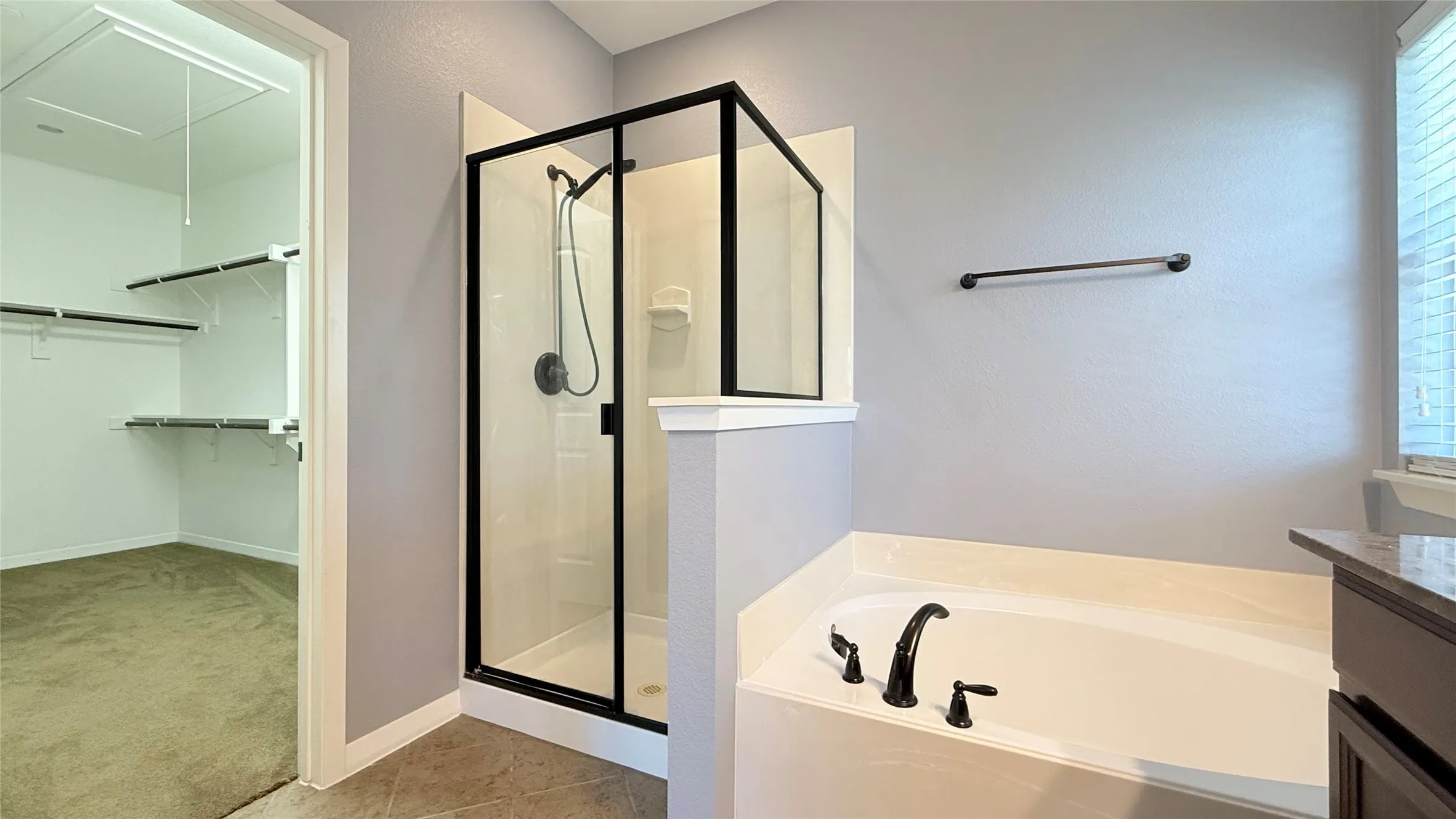 Built-in soaking tub with matte black fixtures, enclosed shower with black frame, built-in shelving, and carpeted flooring
