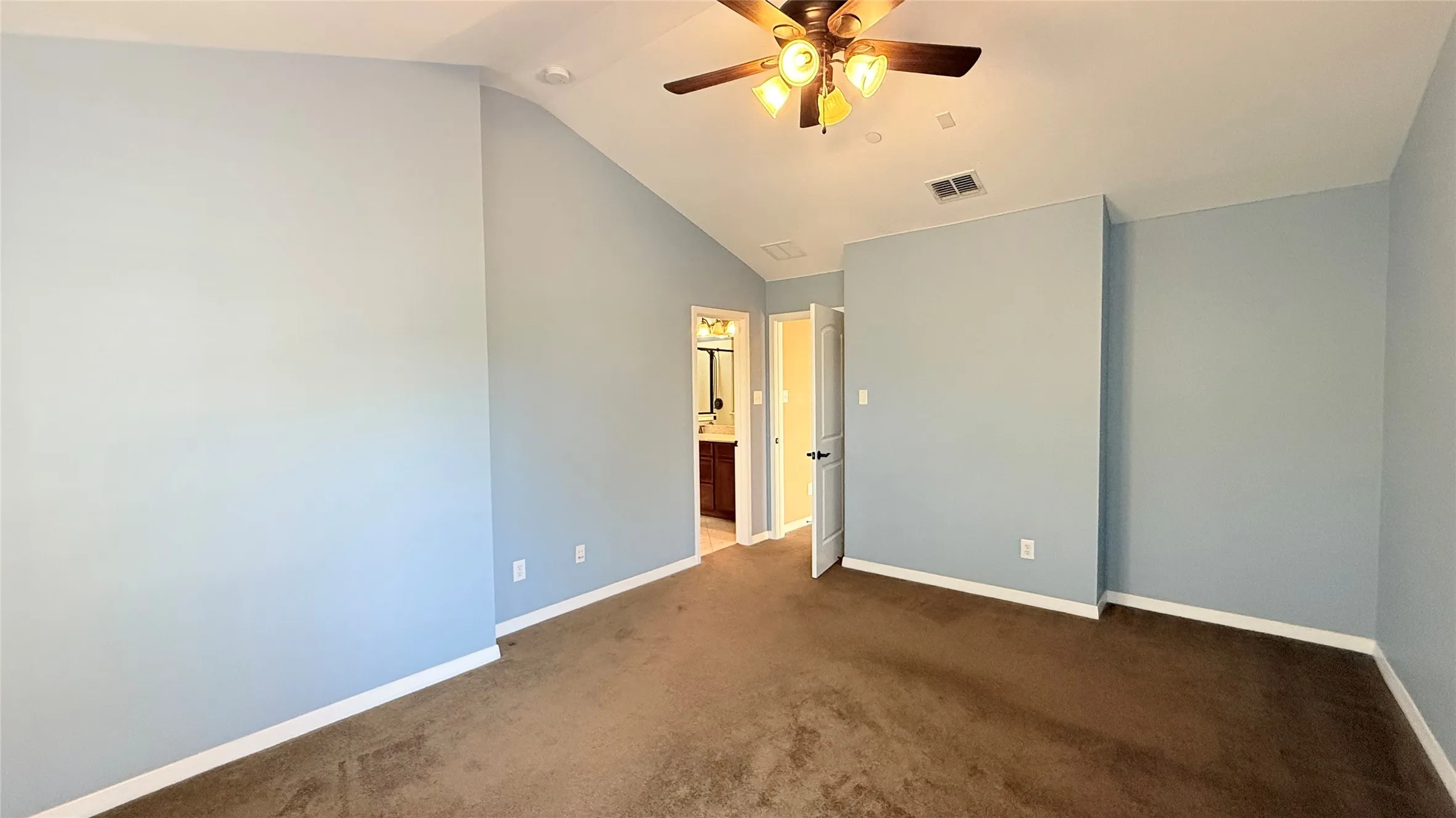 Vaulted ceiling with a ceiling fan light fixture, brown carpet, light blue wall paint, and white trim