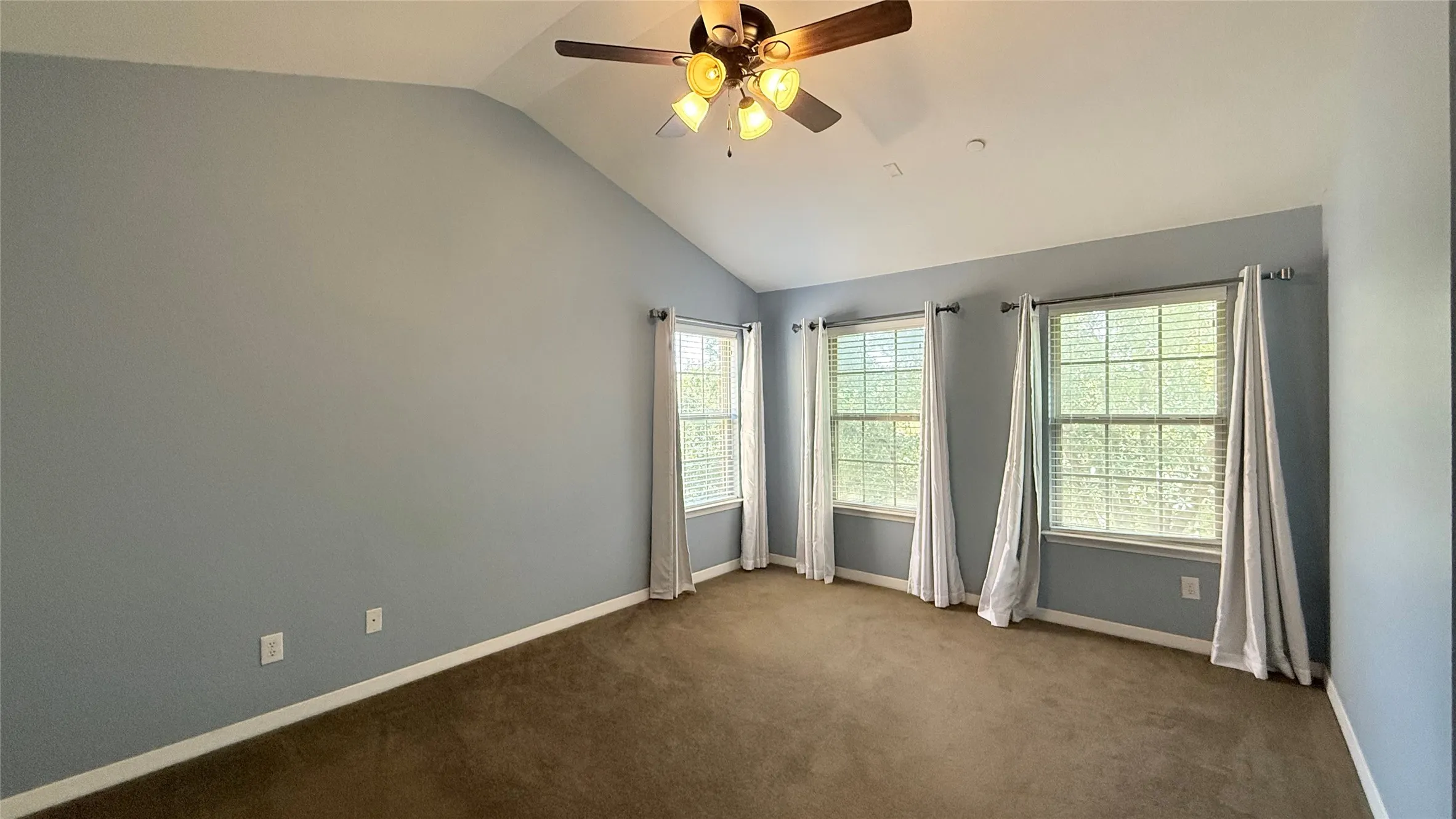 Vaulted ceiling with a ceiling fan, three windows with blinds, light blue walls, and carpet flooring