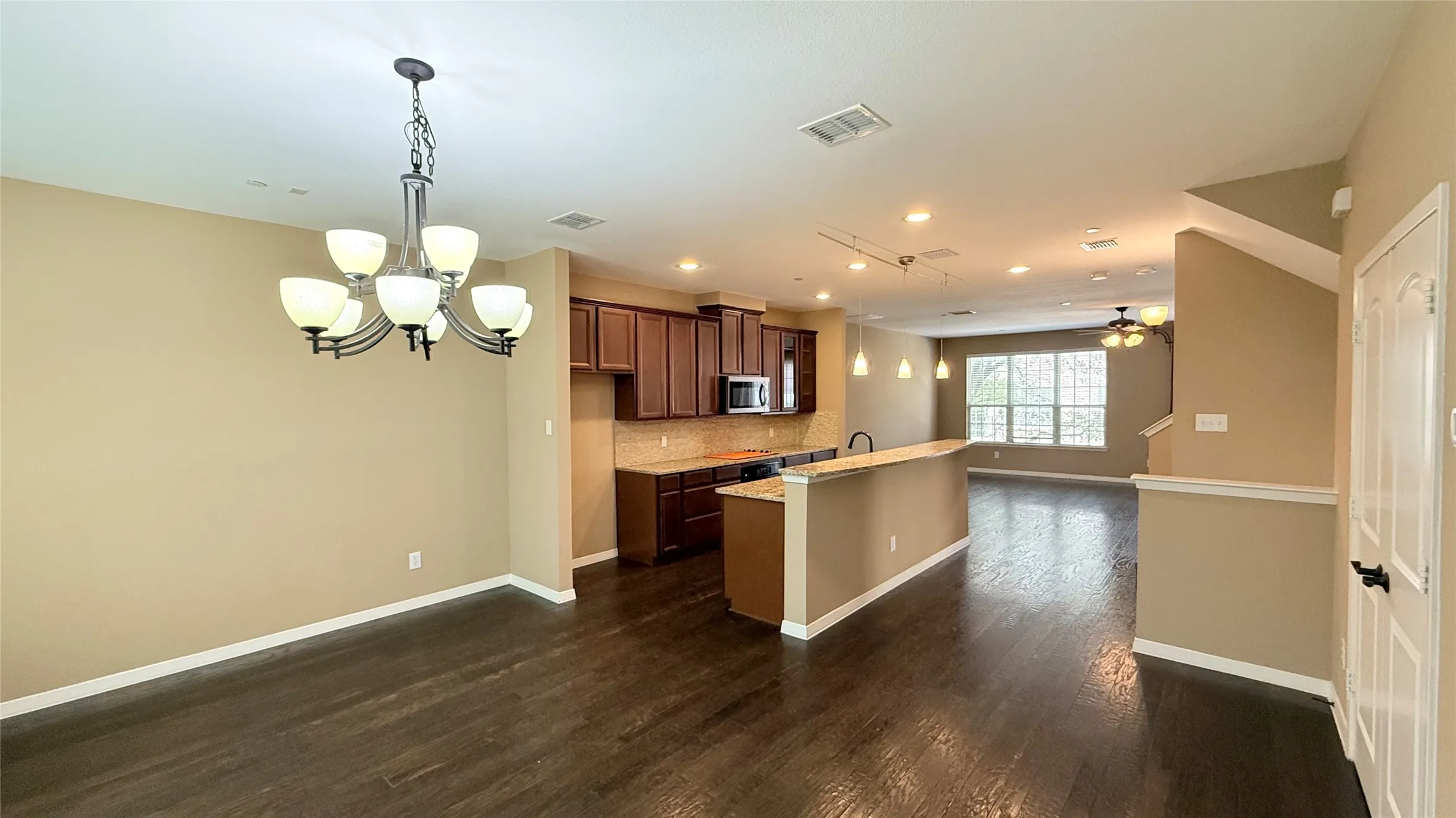 Open-concept living area featuring wood-finish flooring, a kitchen with dark wood cabinetry and integrated appliances, a breakfast bar, and multiple windows