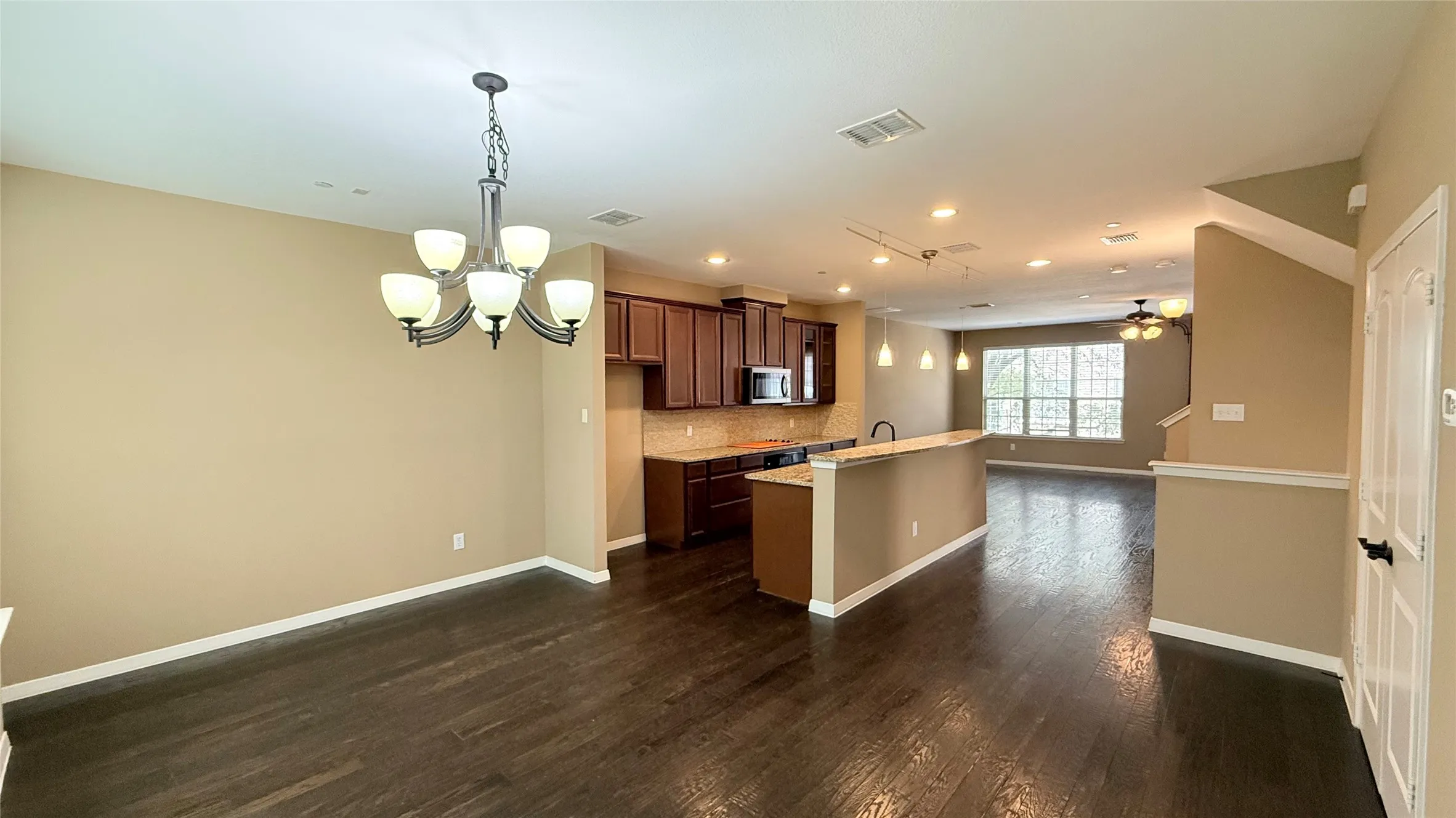Open-concept living area with dark wood-finish flooring, a kitchen featuring dark wood cabinetry and a peninsula, and recessed lighting
