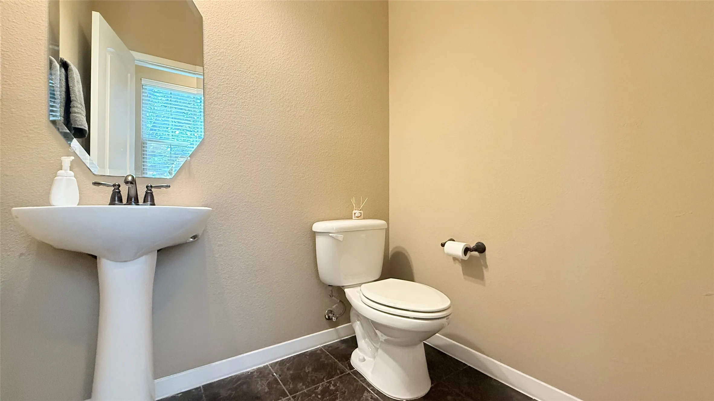 Pedestal sink with dark-toned fixtures, an octagonal mirror, a two-piece toilet, and dark tile flooring