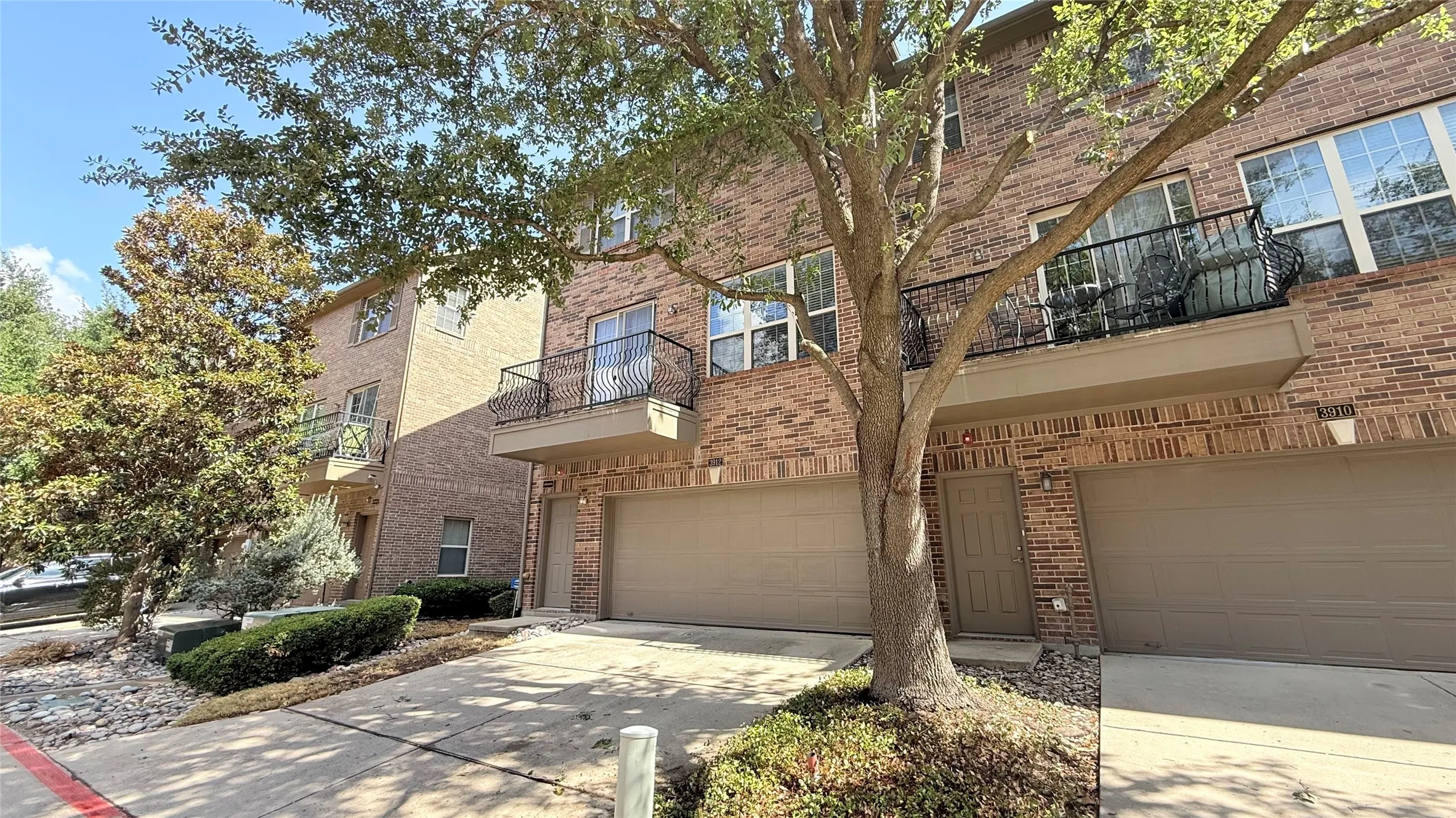 Brick exterior construction with multiple private balconies, attached two-car garages, and mature landscaping