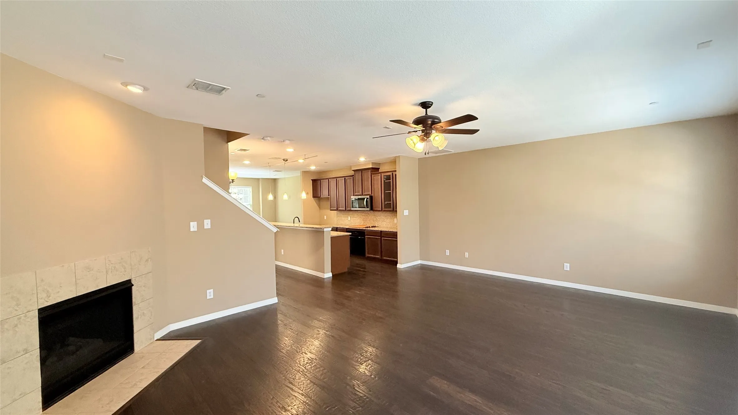 Spacious living area featuring wood-finish flooring, a tiled fireplace, and a ceiling fan