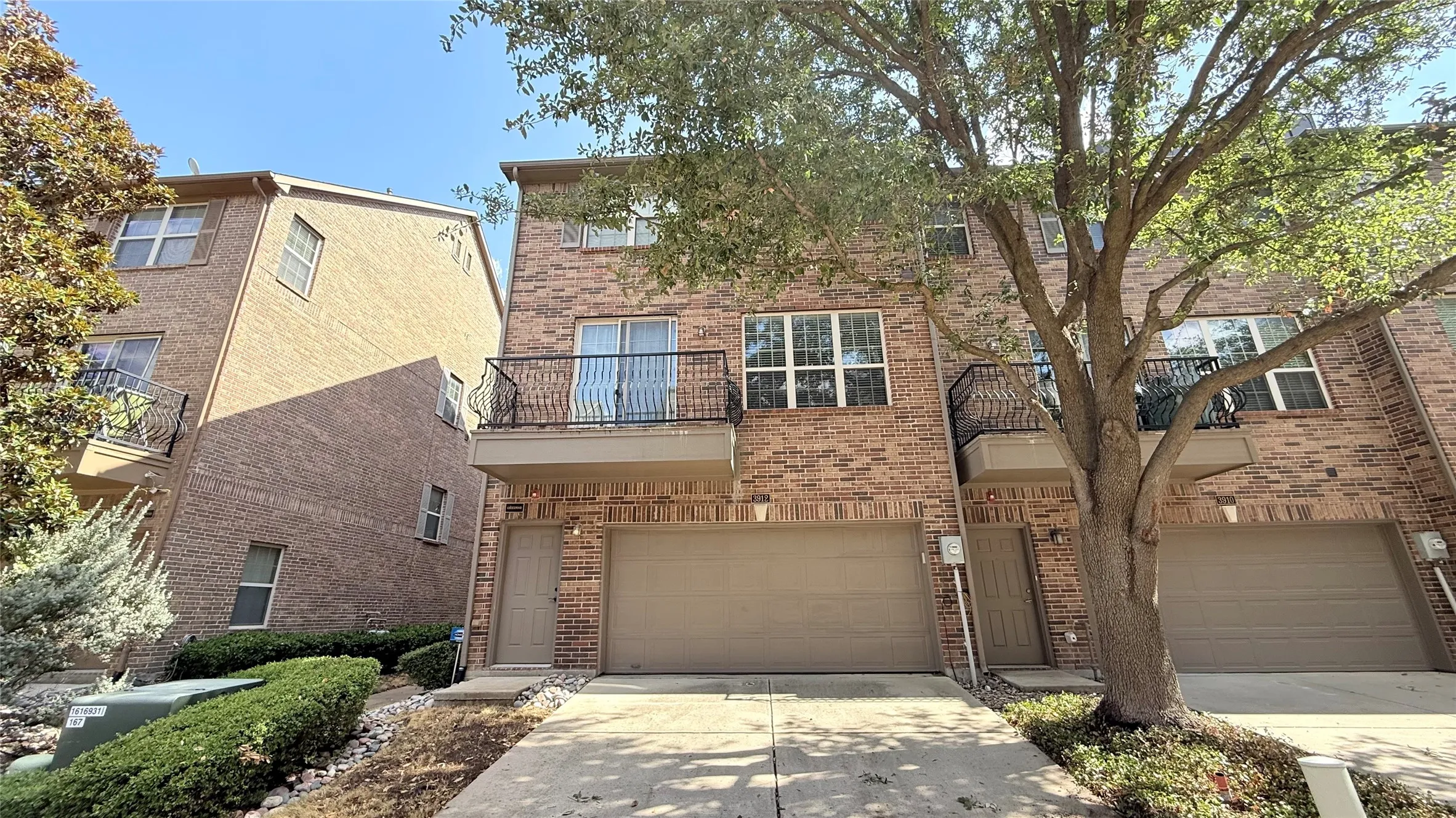 Brick facade with multiple windows, two balconies with wrought iron railings, and an integrated two-car garage