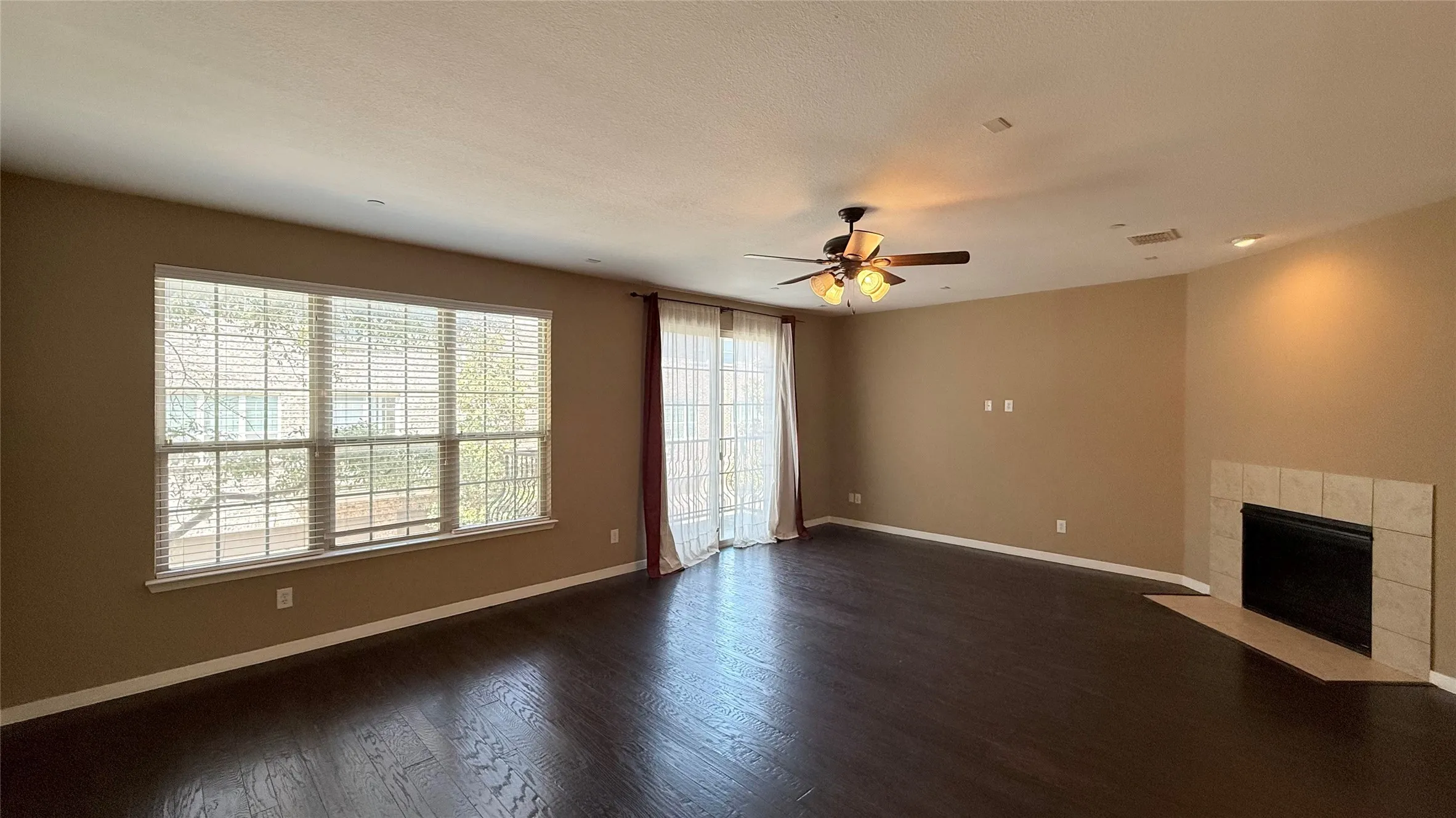 Spacious living area featuring wood-finish flooring, a ceiling fan with integrated lighting, recessed lighting, a fireplace with a tile surround and hearth, and a large window with blinds