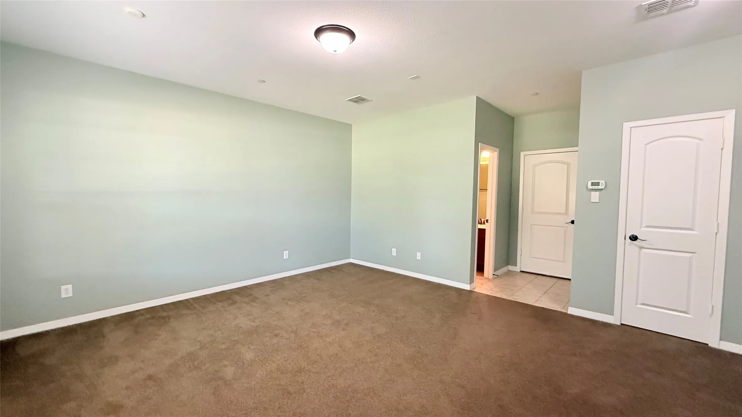 Expansive room featuring light-colored walls and brown carpeting