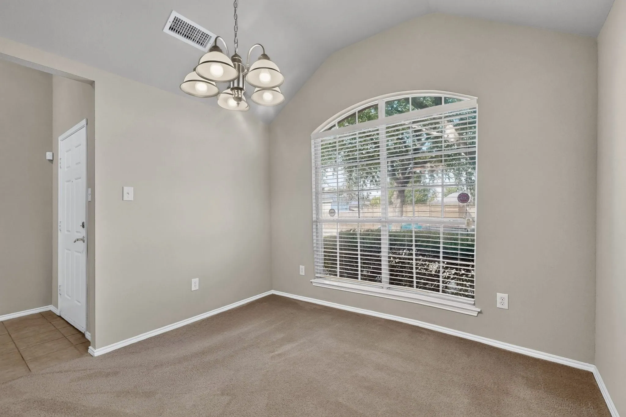 Vaulted ceiling, arched window, five-light chandelier, carpet flooring, paneled door