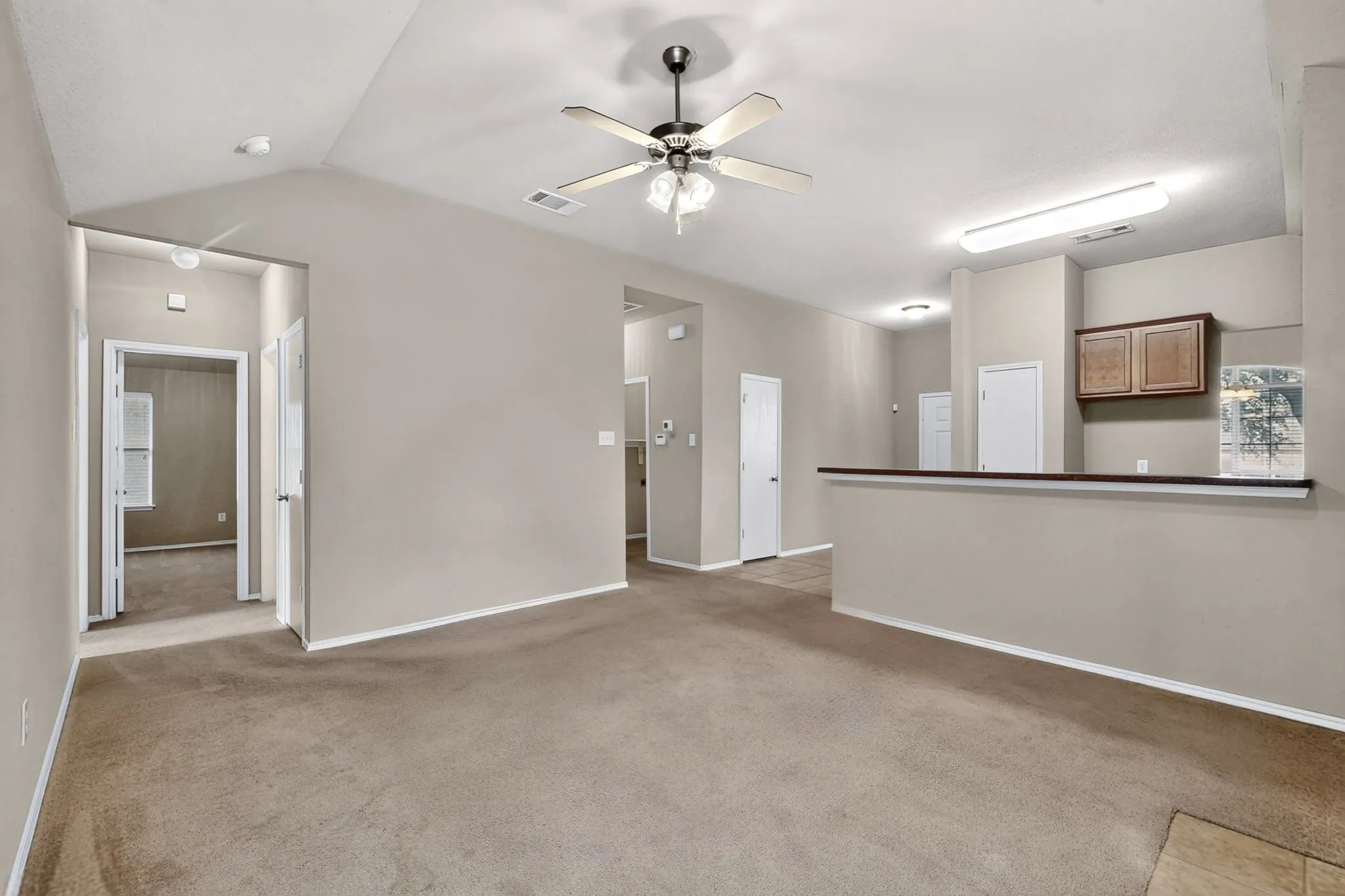 Vaulted ceiling with a ceiling fan, neutral wall tones, carpeted flooring, and a built-in breakfast bar with upper cabinetry