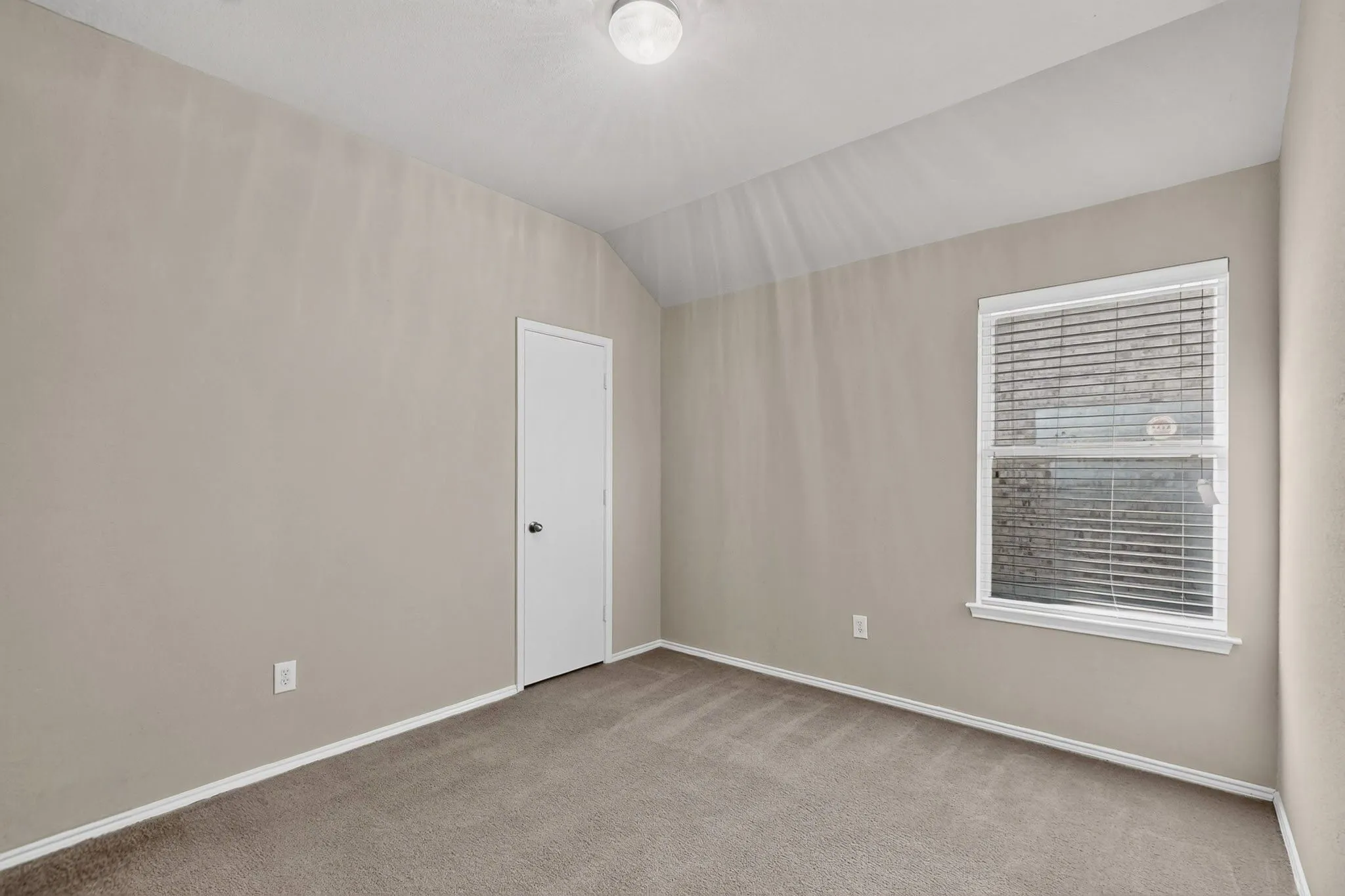 Carpet flooring, neutral wall tones, vaulted ceiling, single window with blinds, and a flush-mount ceiling light