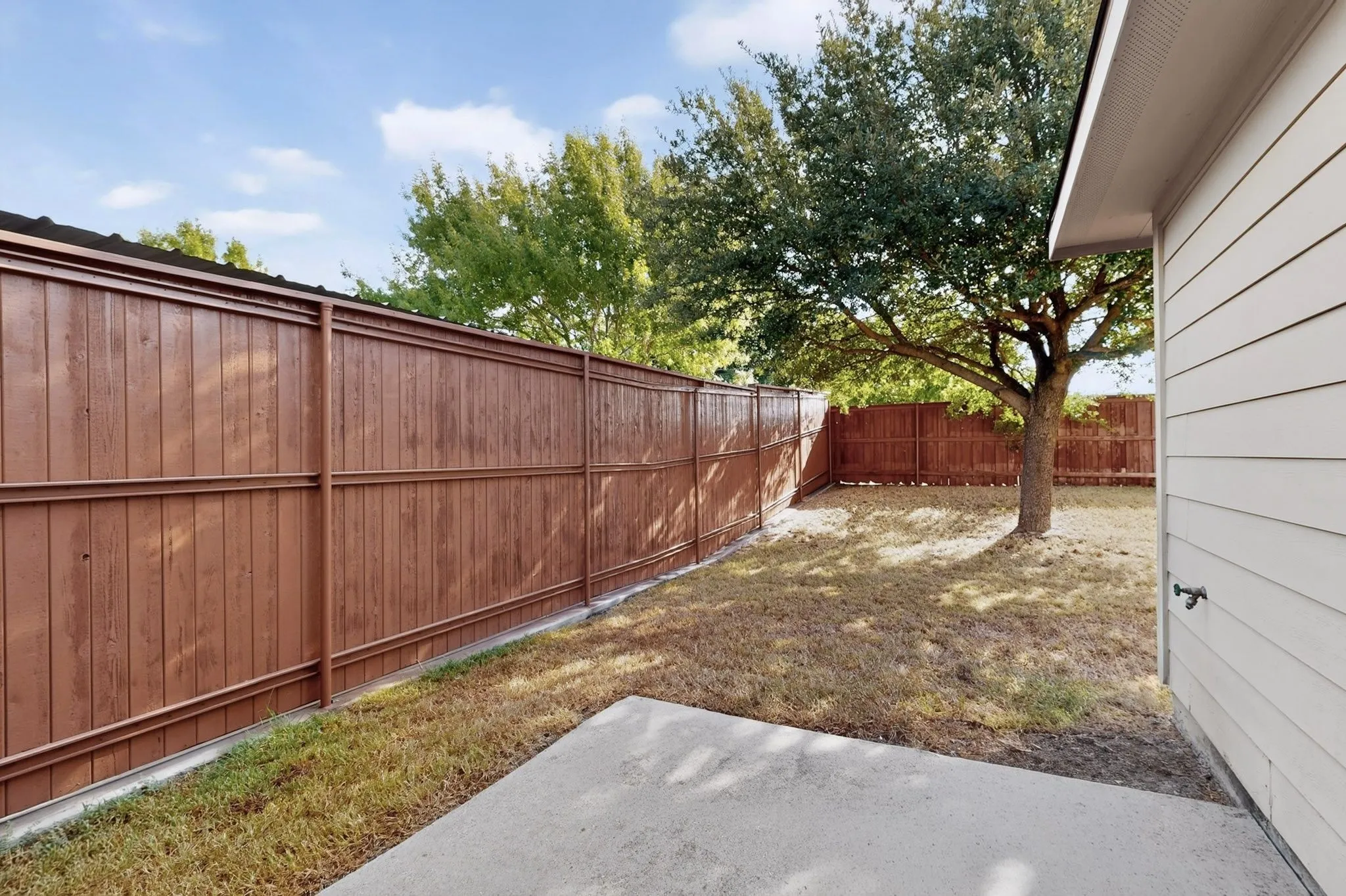Private backyard featuring a concrete patio, wood fencing, and a mature tree