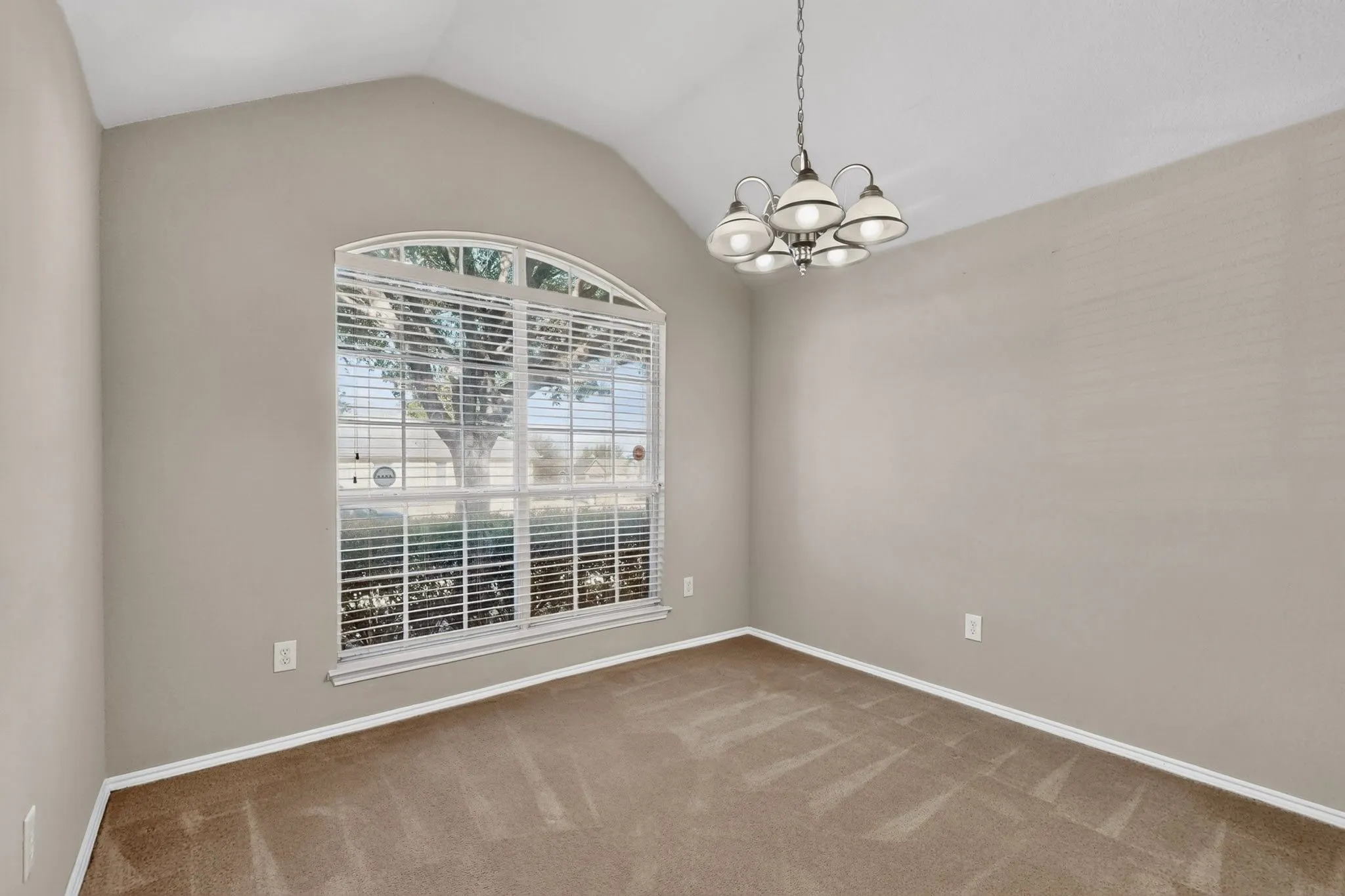 Vaulted ceiling with an arched window, featuring a multi-light chandelier and carpeted flooring