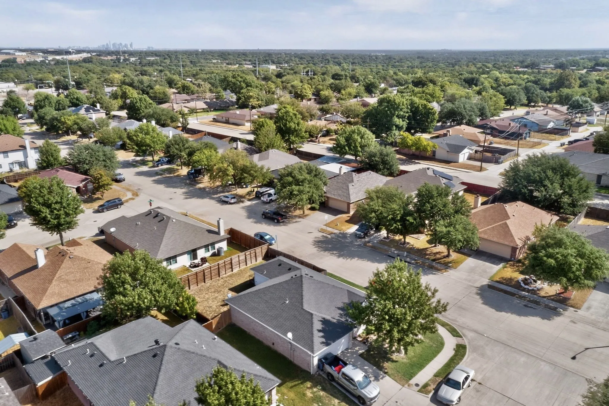 Residential neighborhood with mature trees, paved streets, and a distant skyline