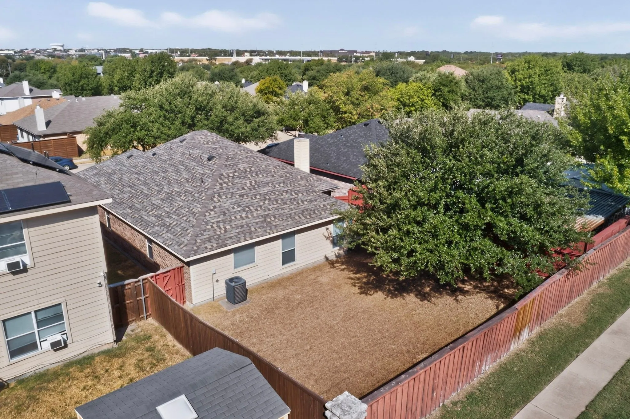 Gable roofline with asphalt shingles, fenced backyard, and established tree canopy