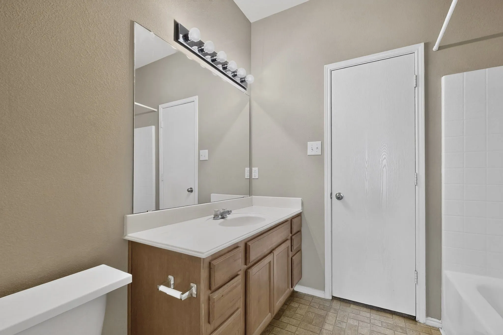 Single vanity with integrated sink, wood-finish cabinetry, and a large wall-mounted mirror