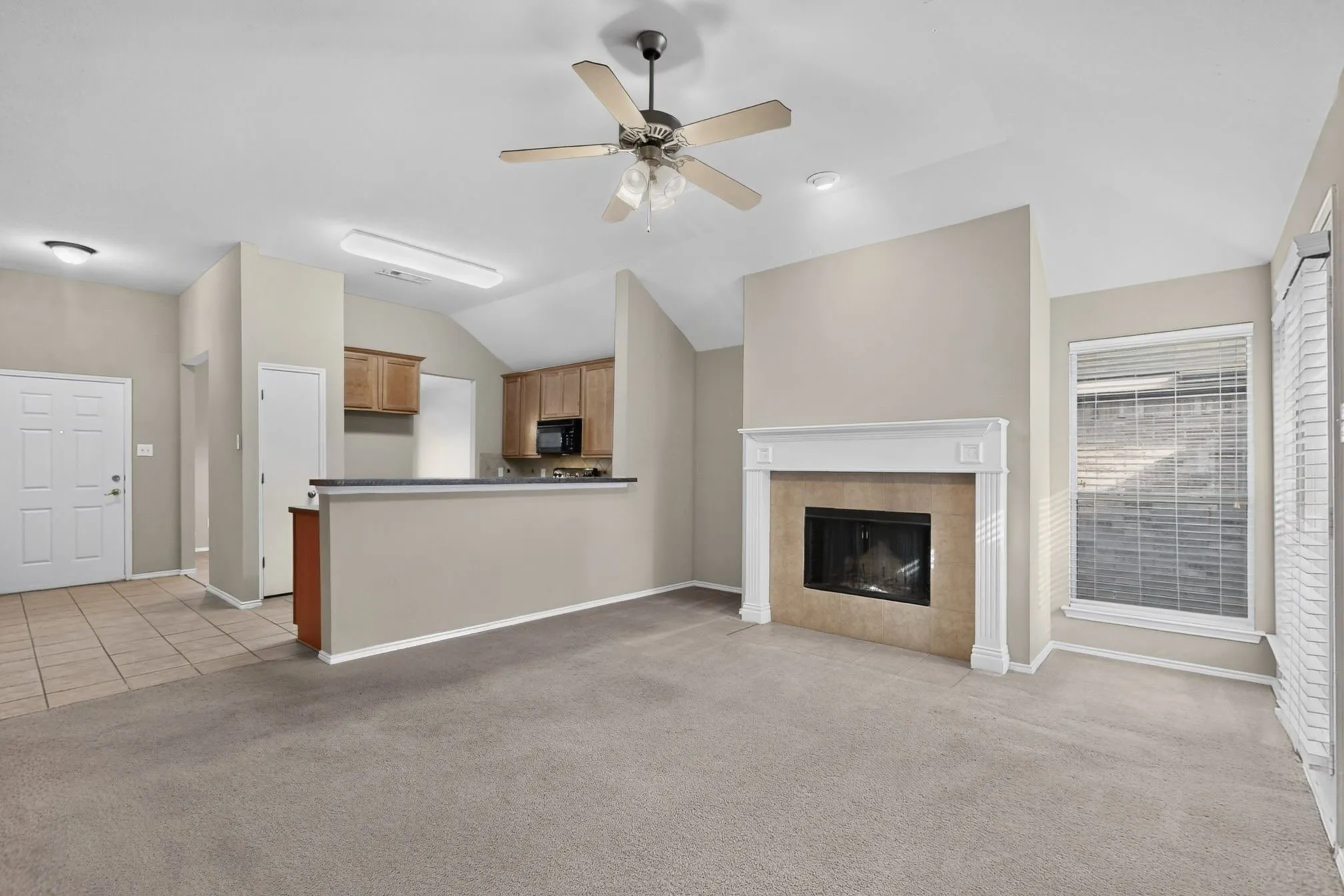 Carpeted living area with a vaulted ceiling, ceiling fan, and decorative fireplace with a stone surround