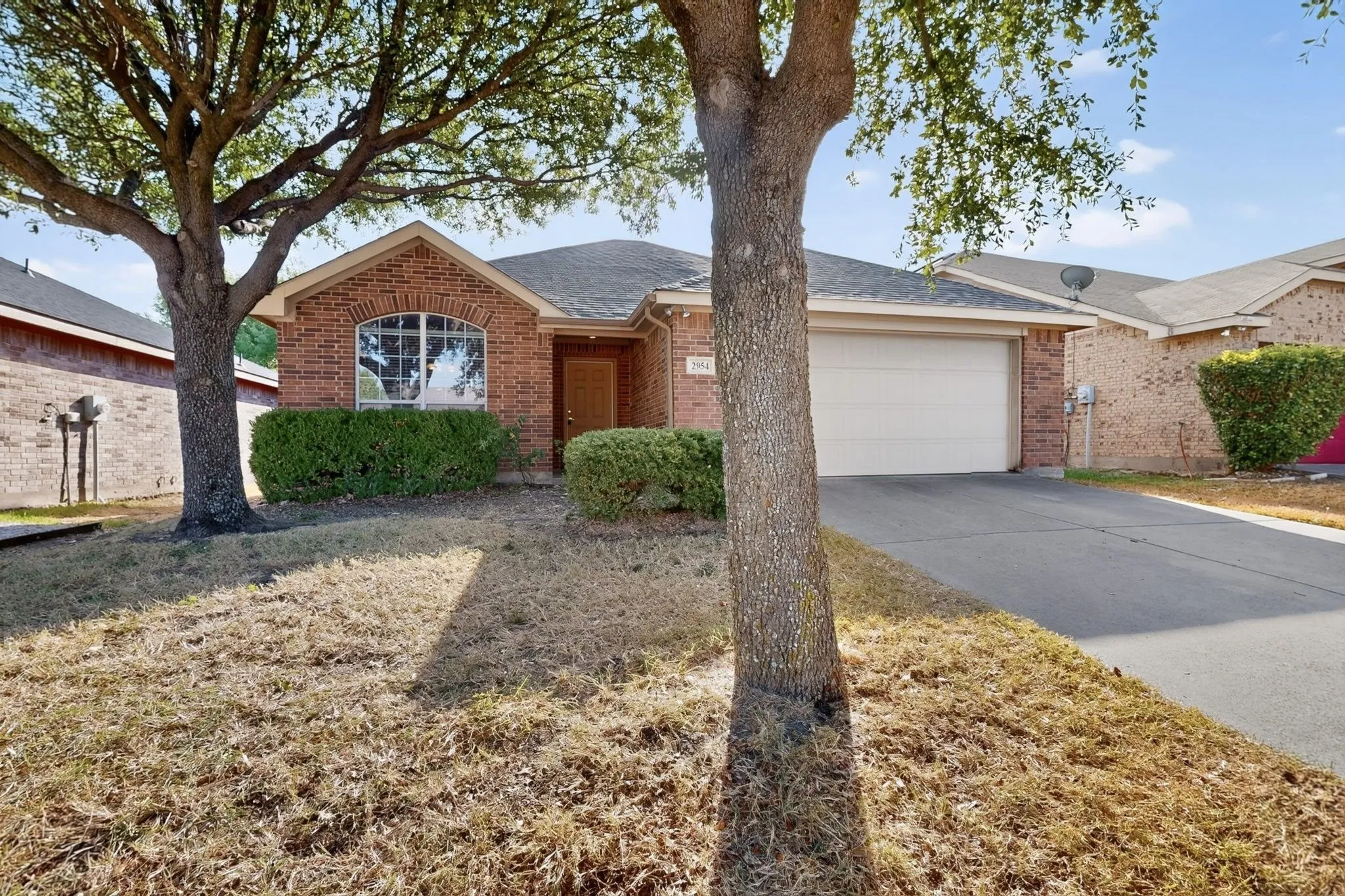 Brick exterior, arched window, attached garage, paved driveway, mature trees