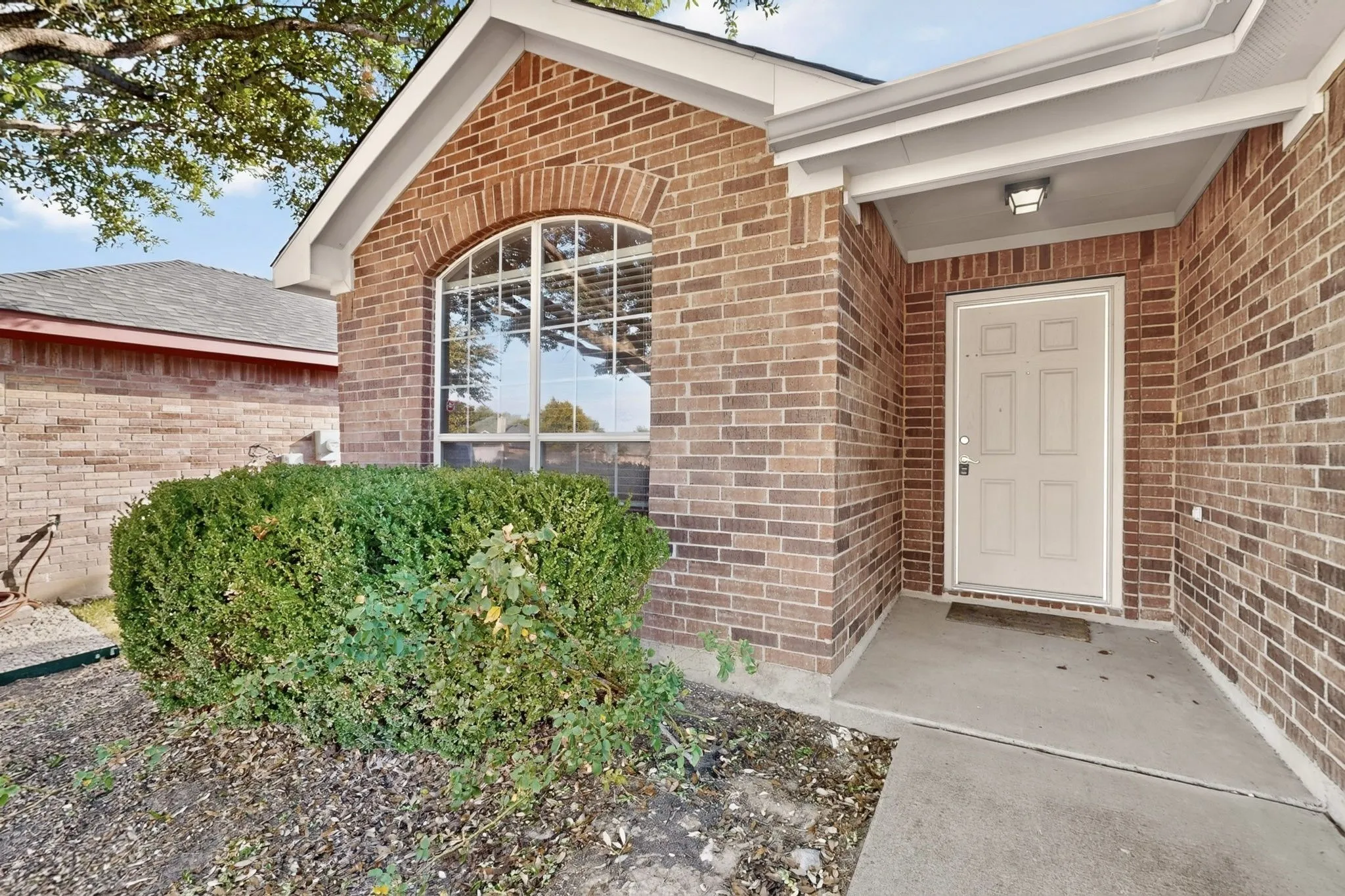 Brick exterior featuring an arched window, covered entryway, and a paneled front door