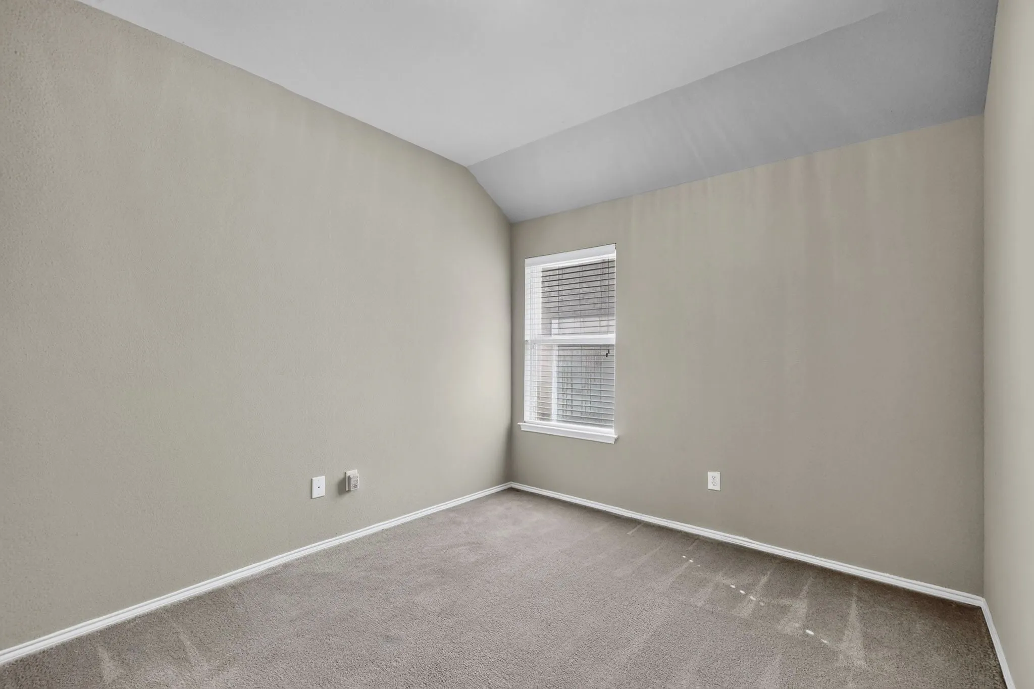 Carpeted flooring, neutral wall tones, window with horizontal blinds, and vaulted ceiling