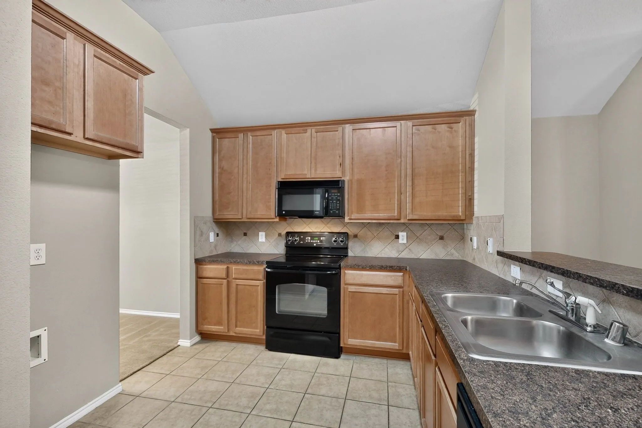 Kitchen featuring wood-finish cabinetry, black appliances, a double basin stainless steel sink, and tile flooring