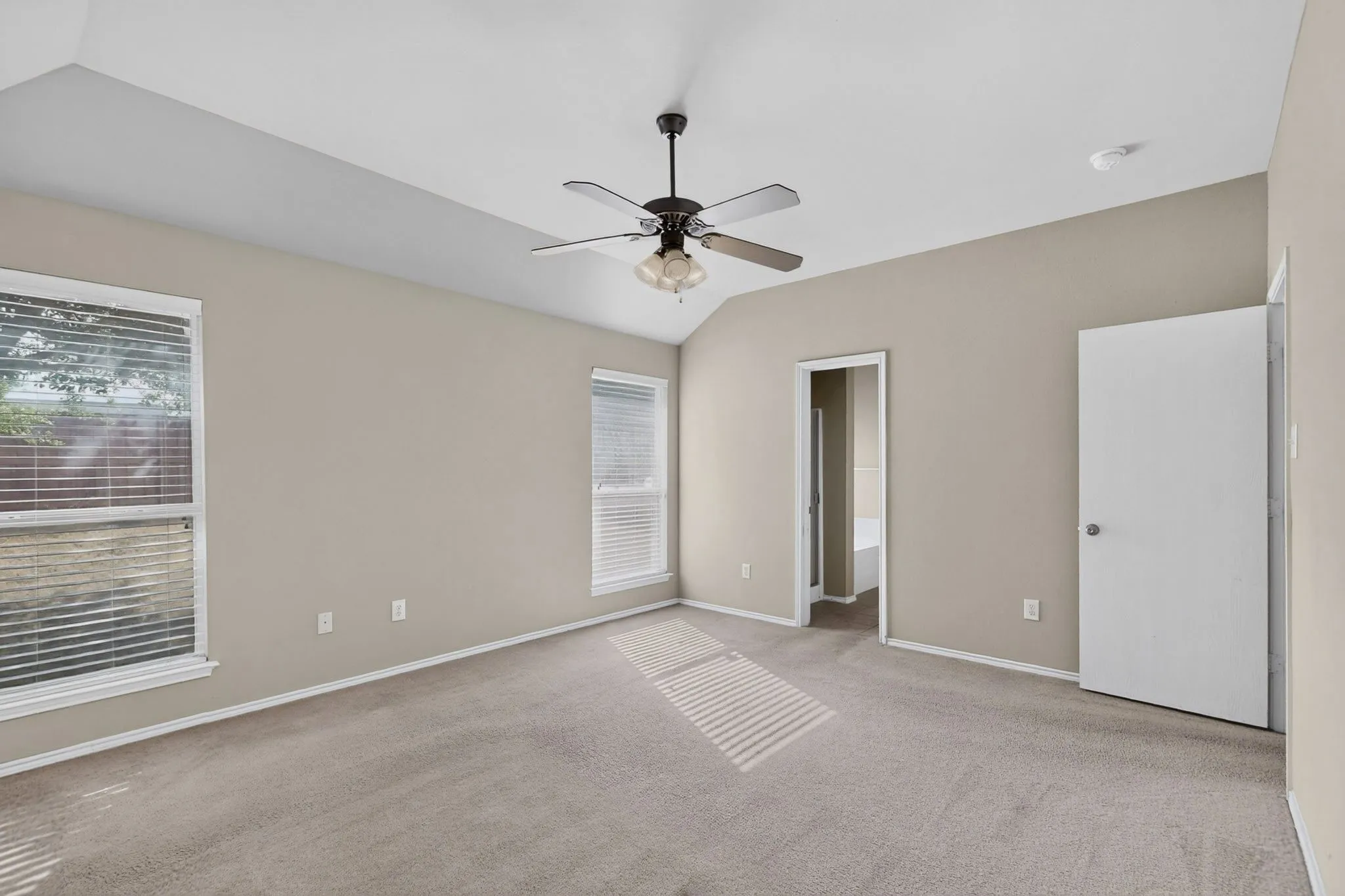 Tray ceiling with a ceiling fan light fixture, dual windows with blinds, and neutral carpeting