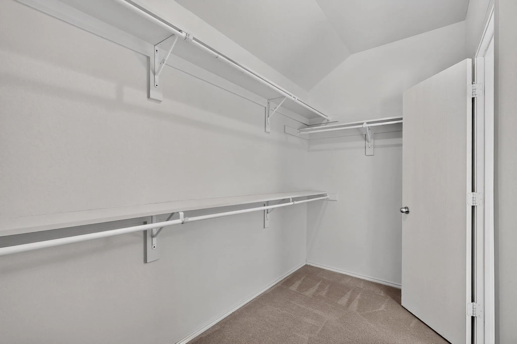 Walk-in closet with multiple white wire shelving units, white hanging rods, and light-toned carpeting