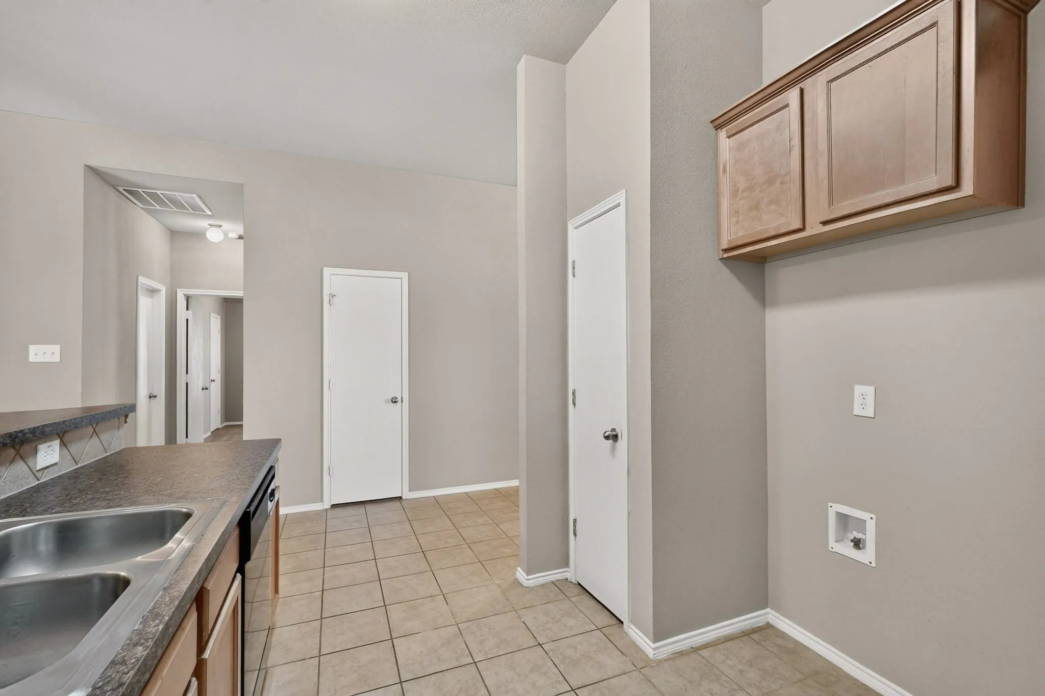 Kitchen area with a double basin stainless steel sink, dark countertops, and light wood-finish cabinetry