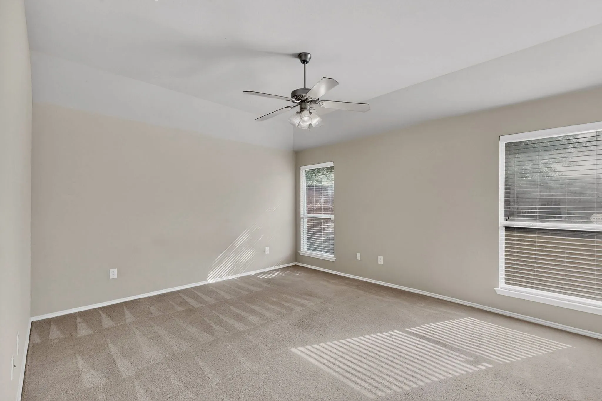 Vaulted ceiling with an attached ceiling fan, two windows with blinds, and neutral carpeting