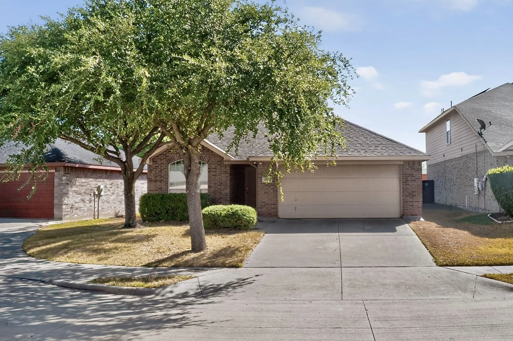 Brick exterior with an attached garage, paved driveway, and mature landscaping