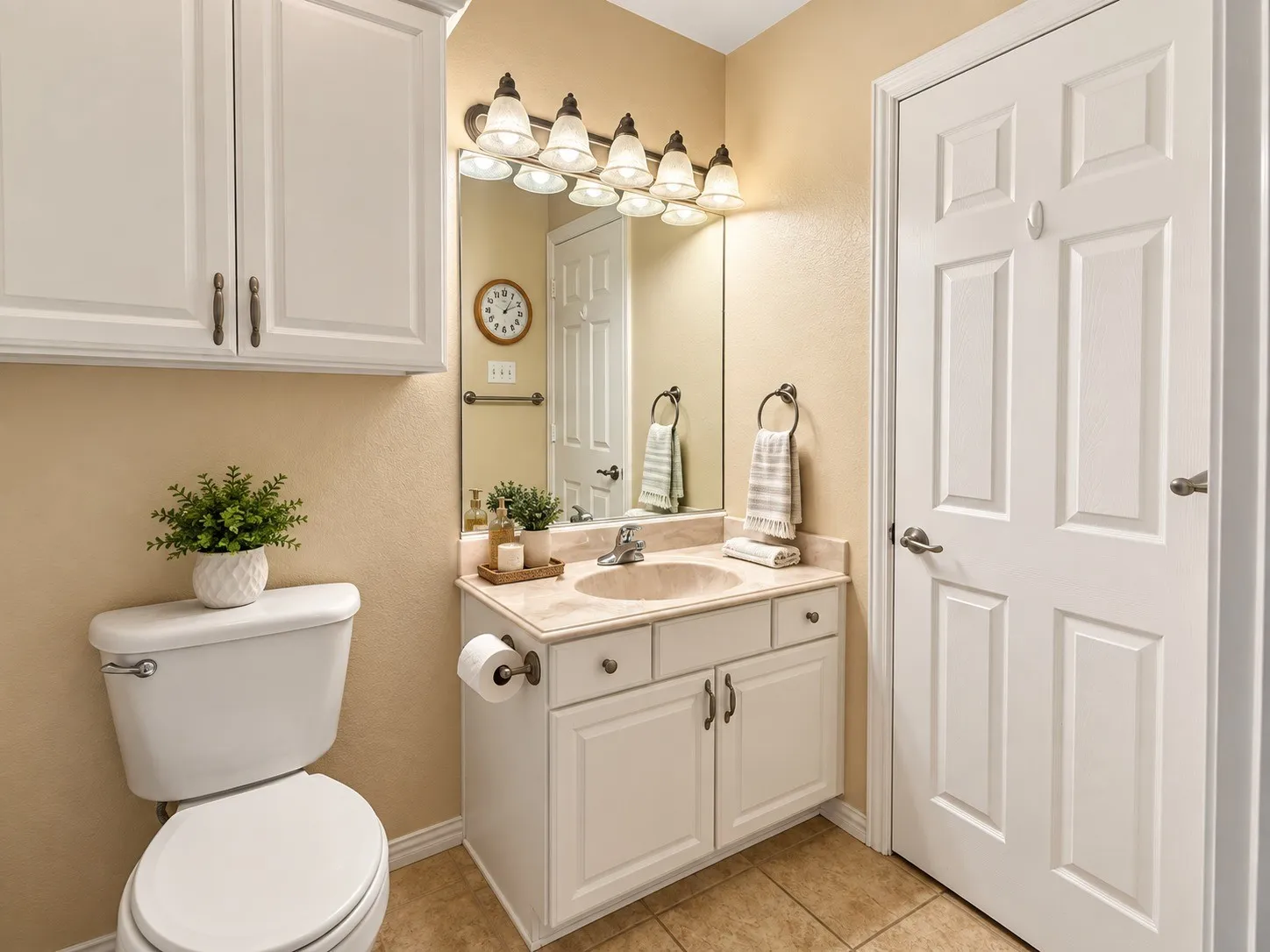 Vanity with integrated sink and countertop, white cabinetry with bronze-finish hardware, built-in medicine cabinet, ceramic tile flooring, and a six-panel door