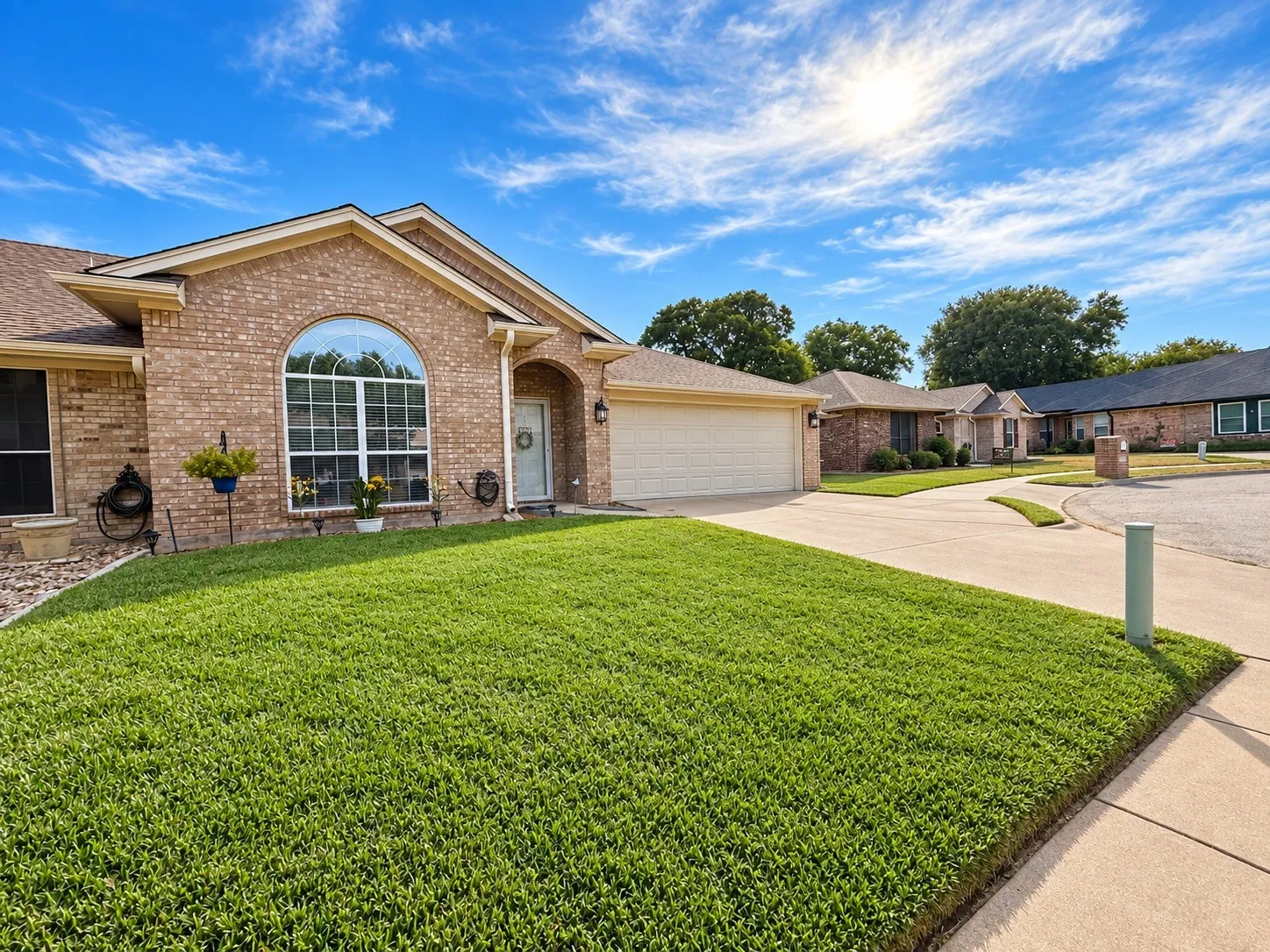 Brick facade with arched window, attached garage, concrete driveway, and front lawn